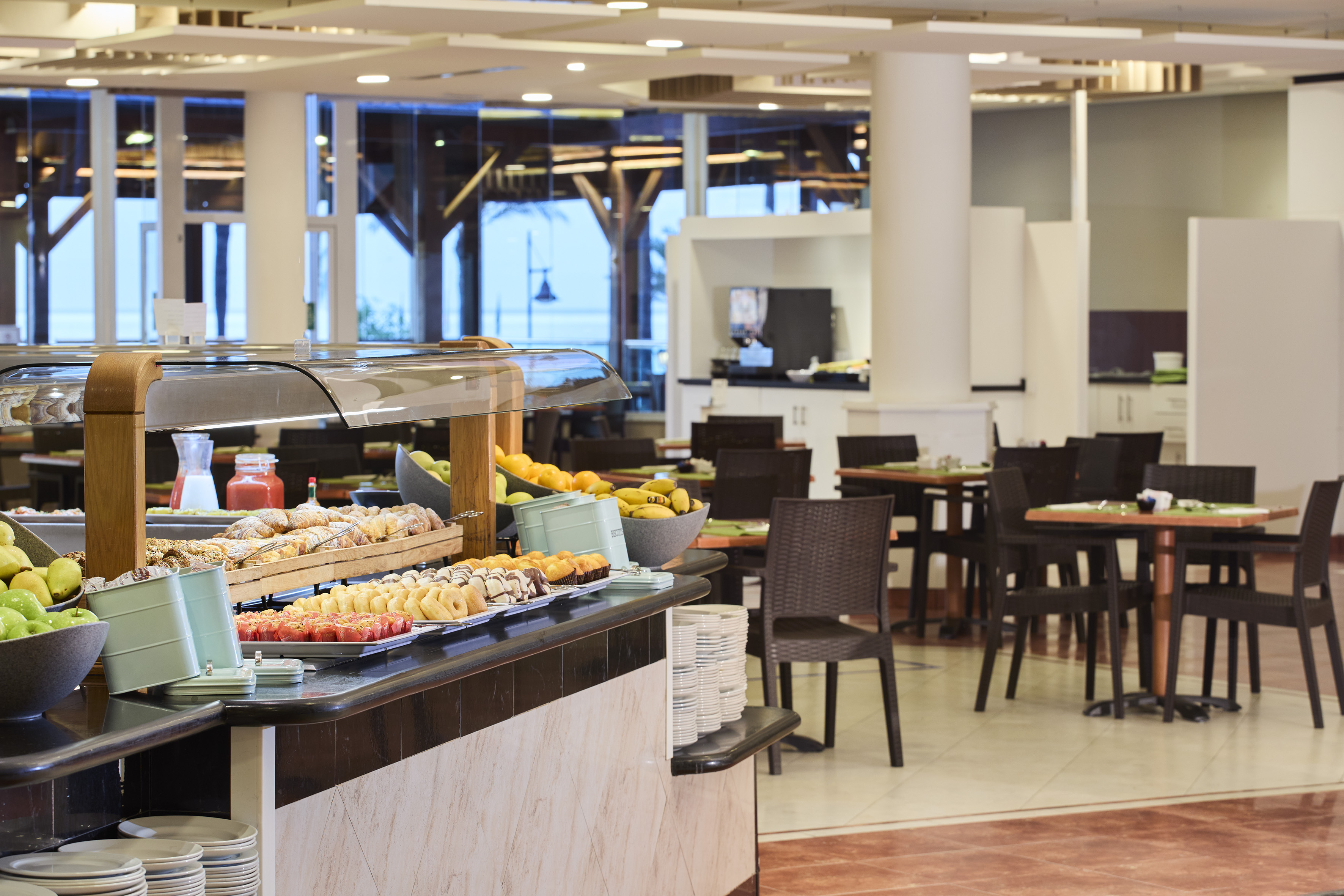 Hotel restaurant buffet with fresh fruit, pastries, and dining tables.