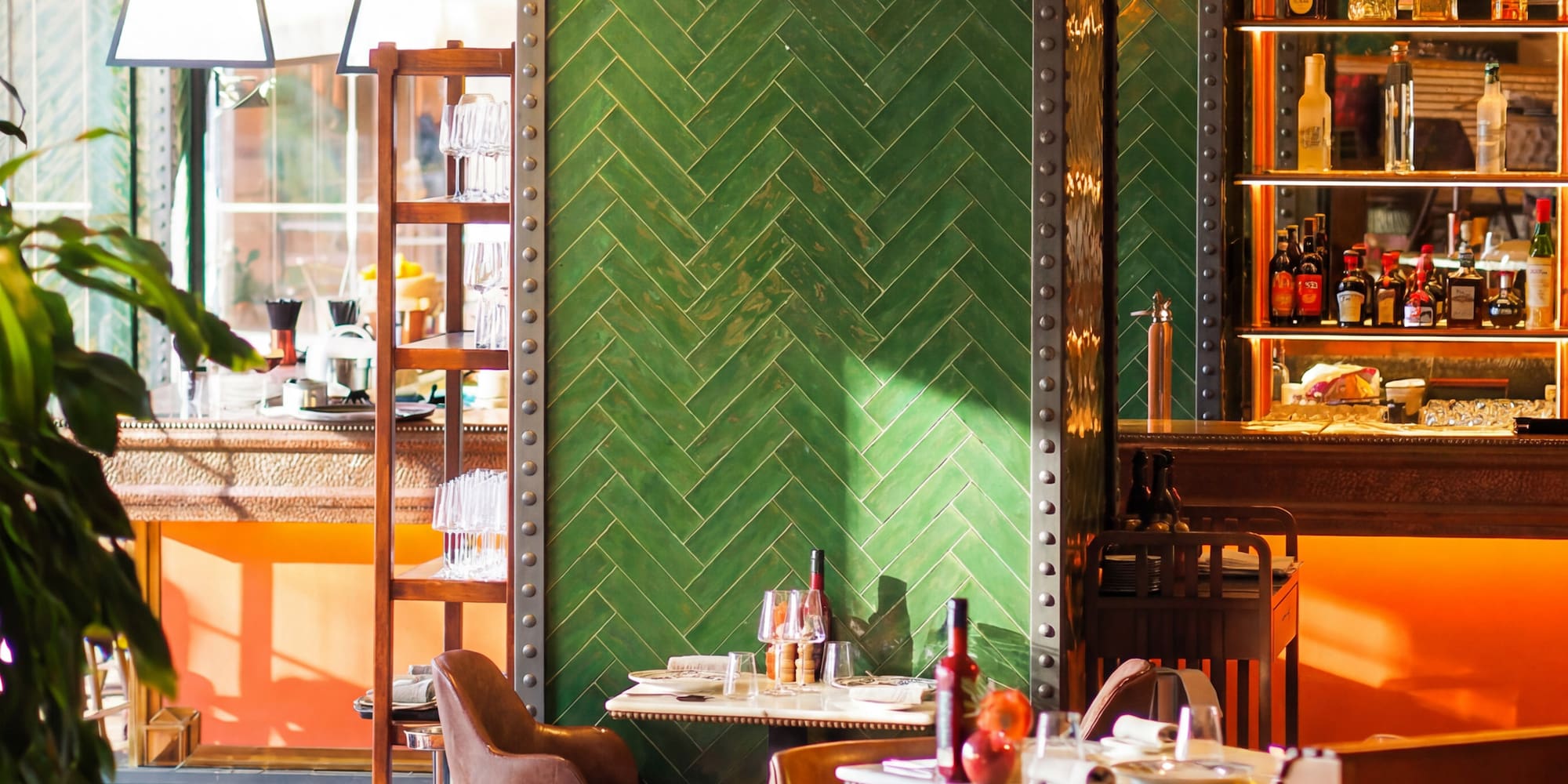Restaurant interior with green herringbone tiles, brown leather chairs, and bar.