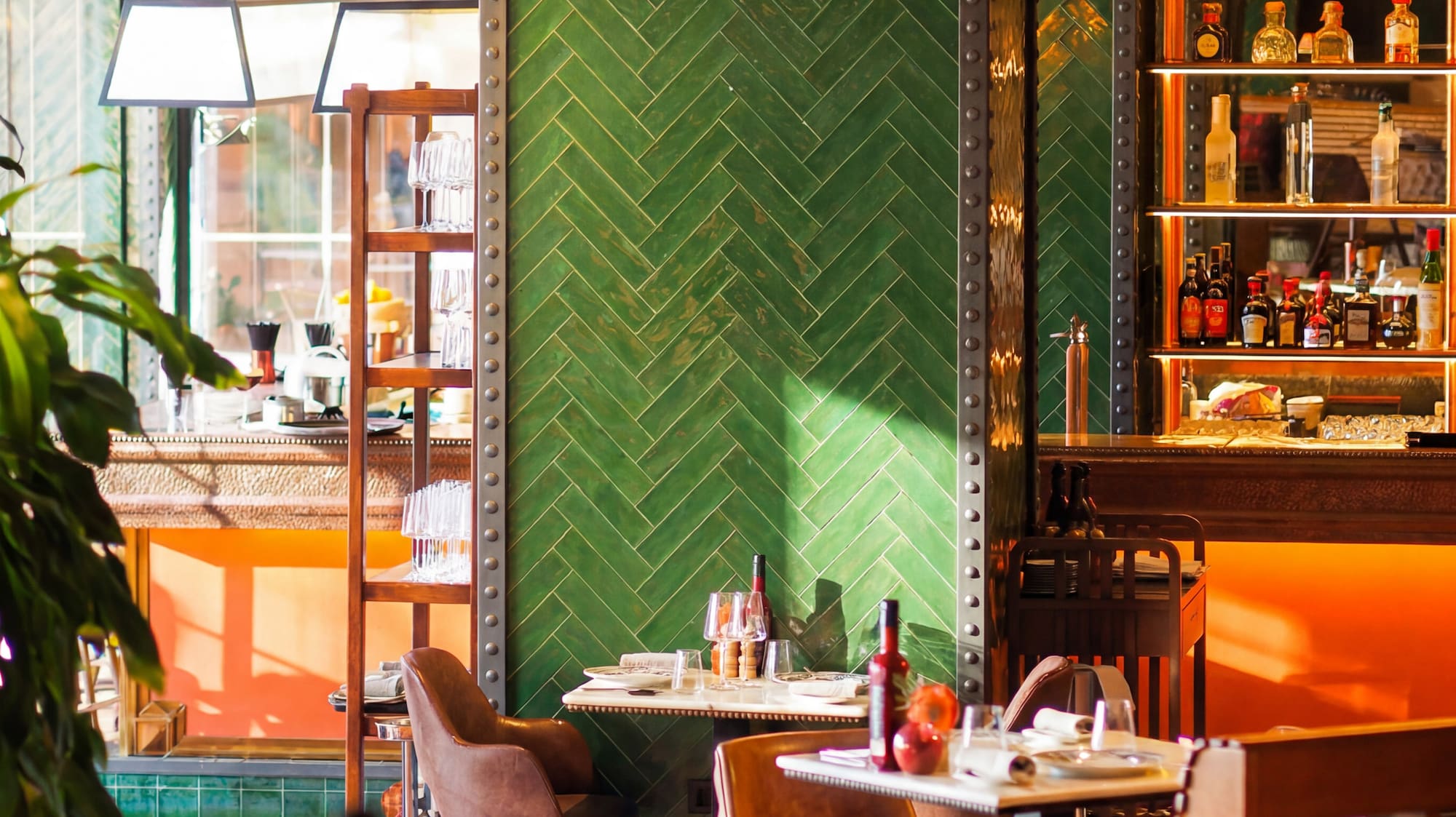 Restaurant interior with green herringbone tiles, brown leather chairs, and bar.