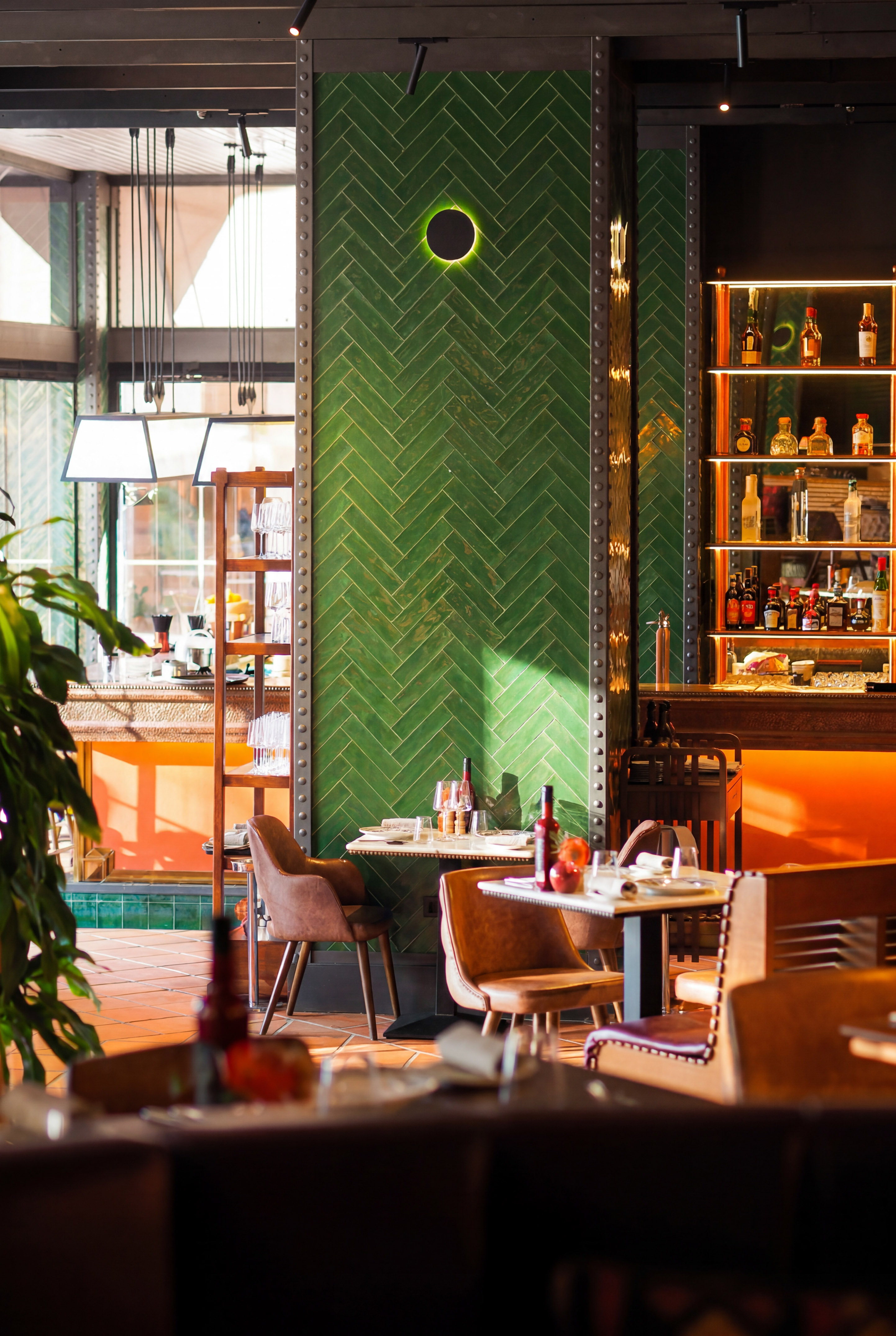 Restaurant interior with green herringbone tiles, brown leather chairs, and bar.