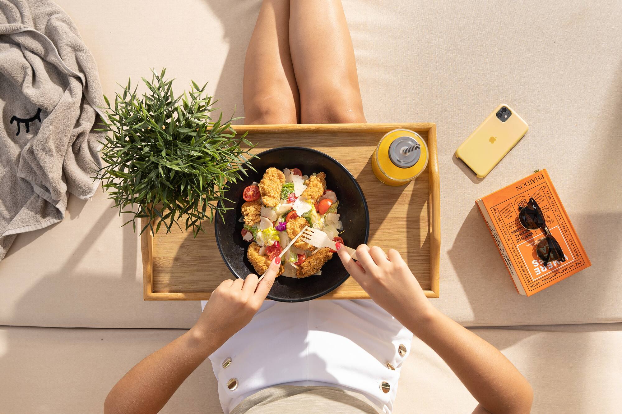 Woman enjoying fresh chicken salad and juice on a sunny outdoor lounge.