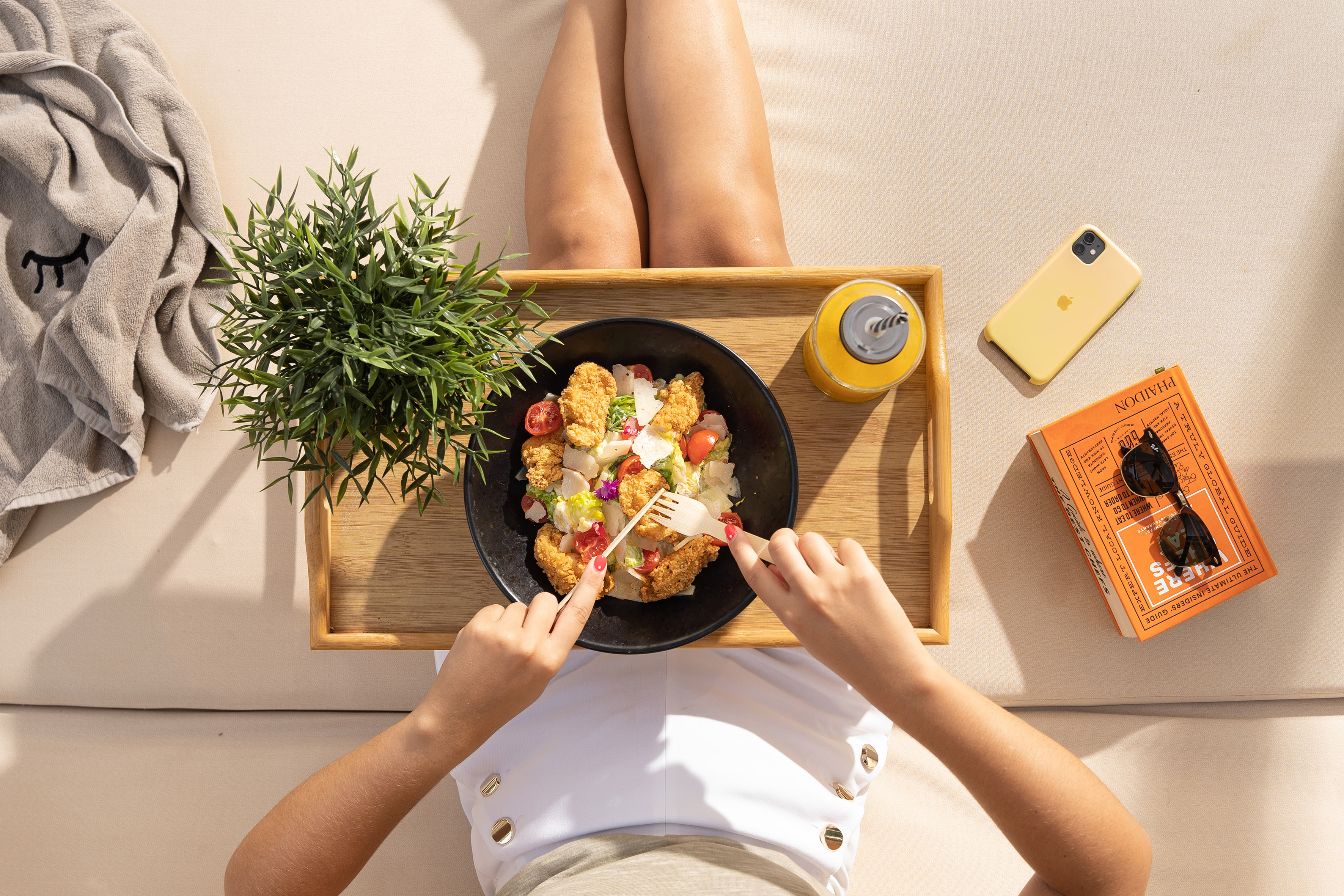 Woman enjoying fresh chicken salad and juice on a sunny outdoor lounge.