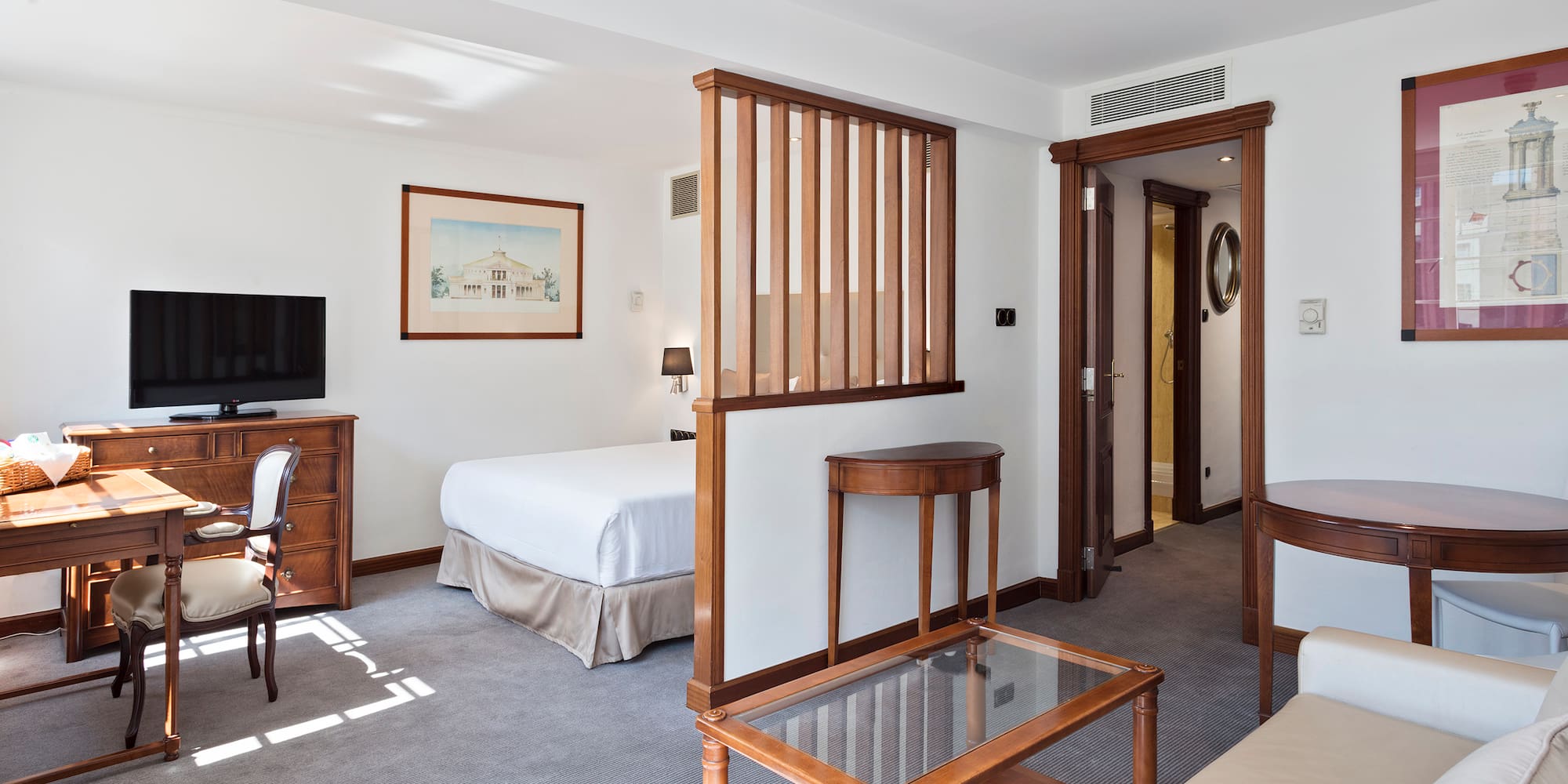 Elegant hotel suite with bedroom, living area, and modern wood partition.