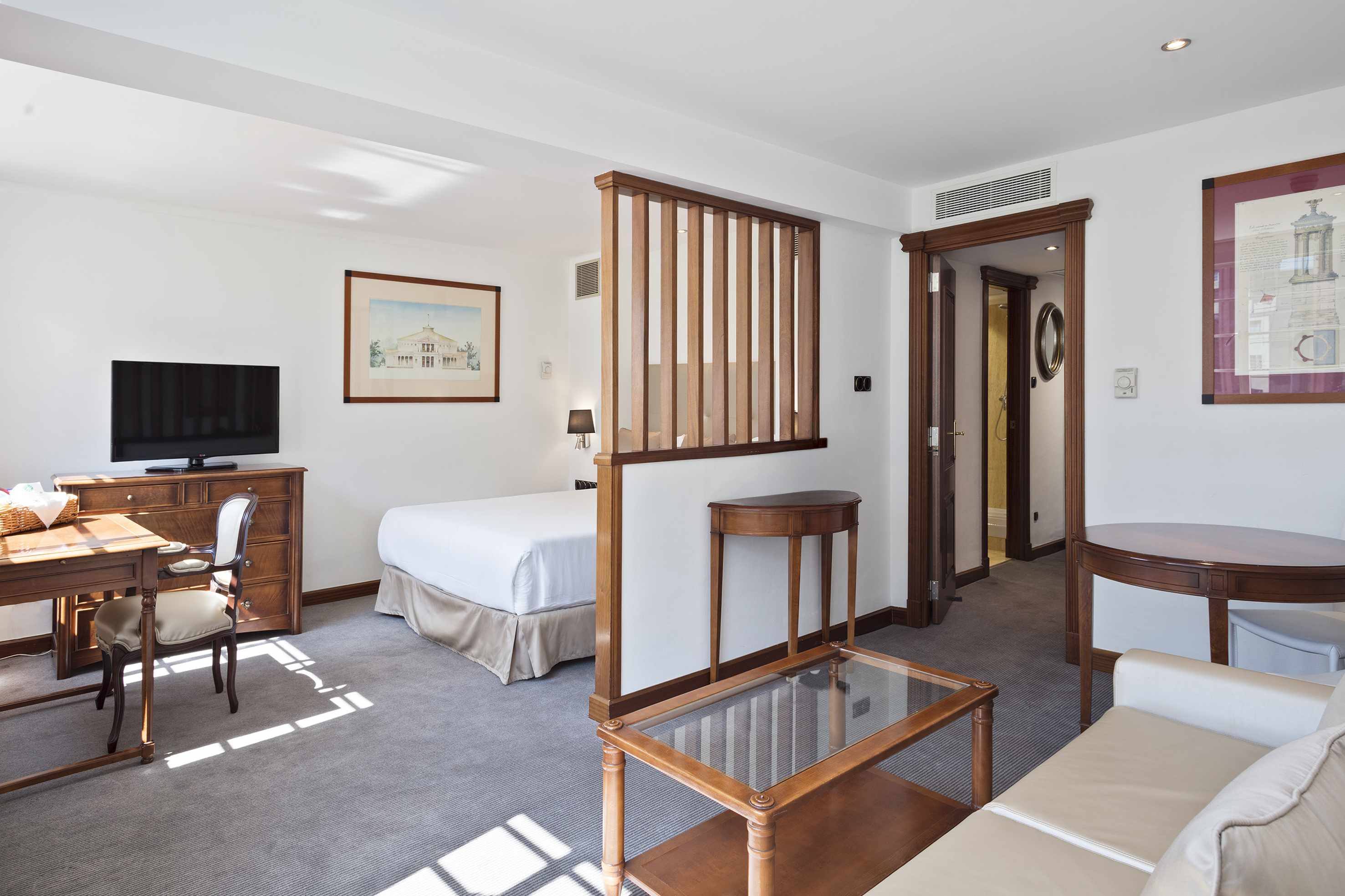 Elegant hotel suite with bedroom, living area, and modern wood partition.