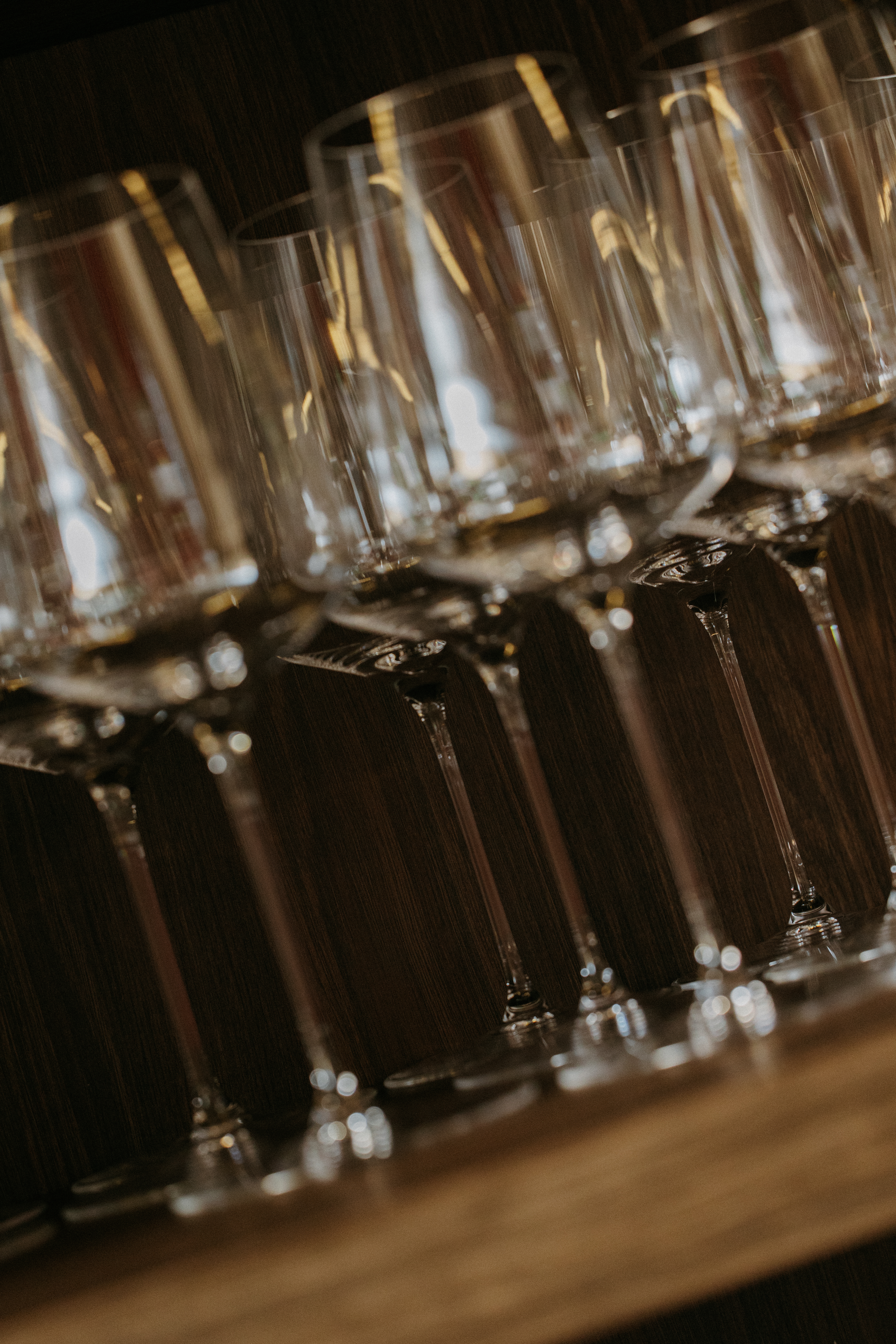 Filas de copas de cristal para vino, boca abajo en estante de madera oscuro.