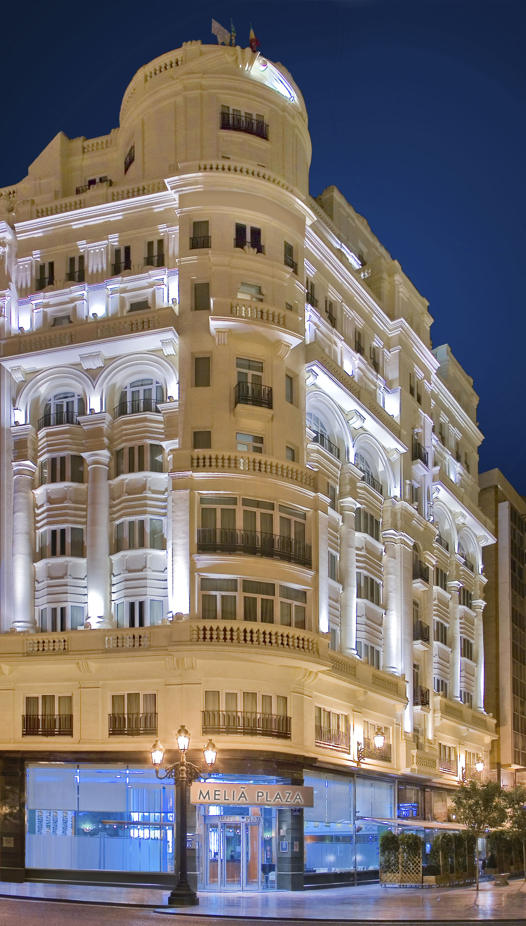 Illuminated Melia Plaza hotel building at night with classic architecture.
