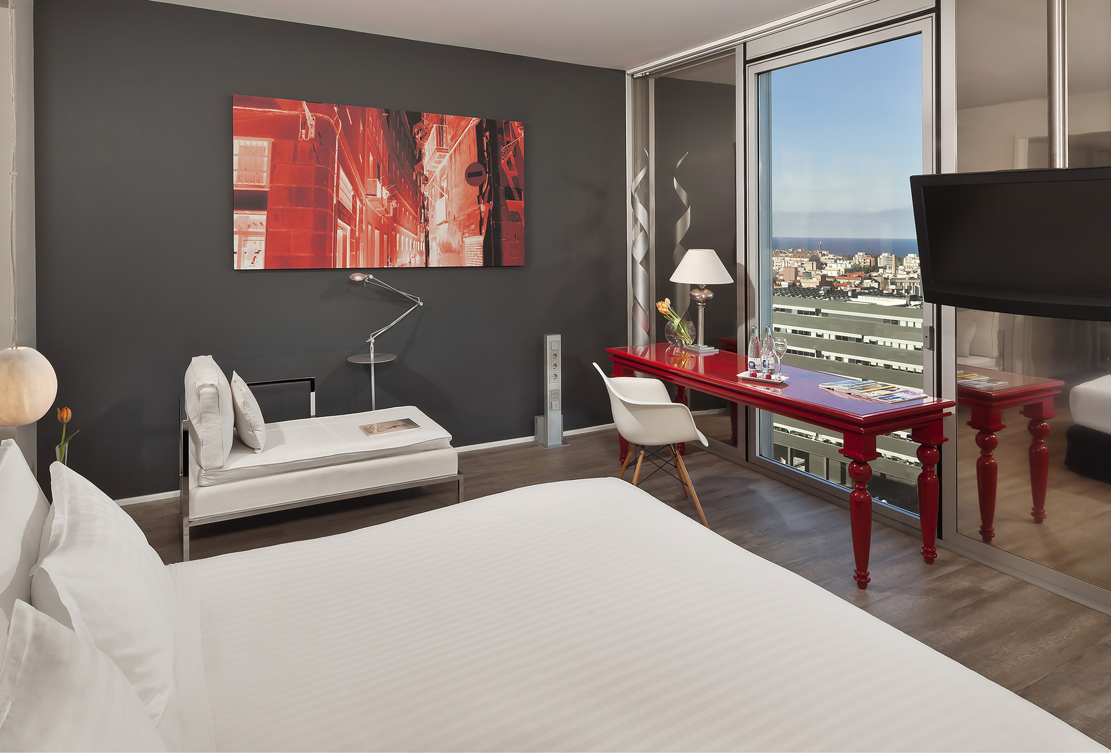 Luxury hotel room with modern decor, city view, red desk, and white bed.