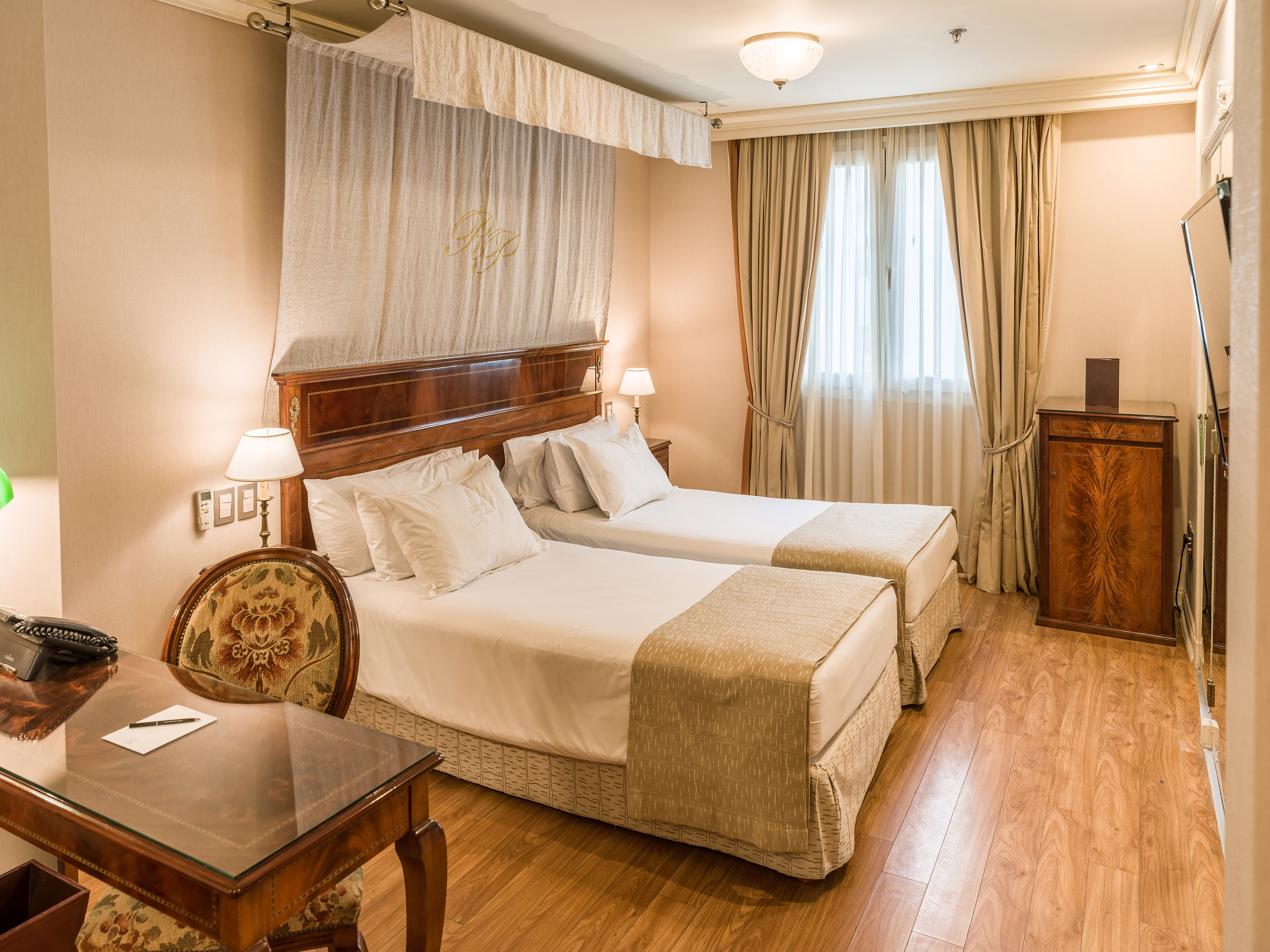 Elegant hotel room with two twin beds, wooden desk, and classic decor.