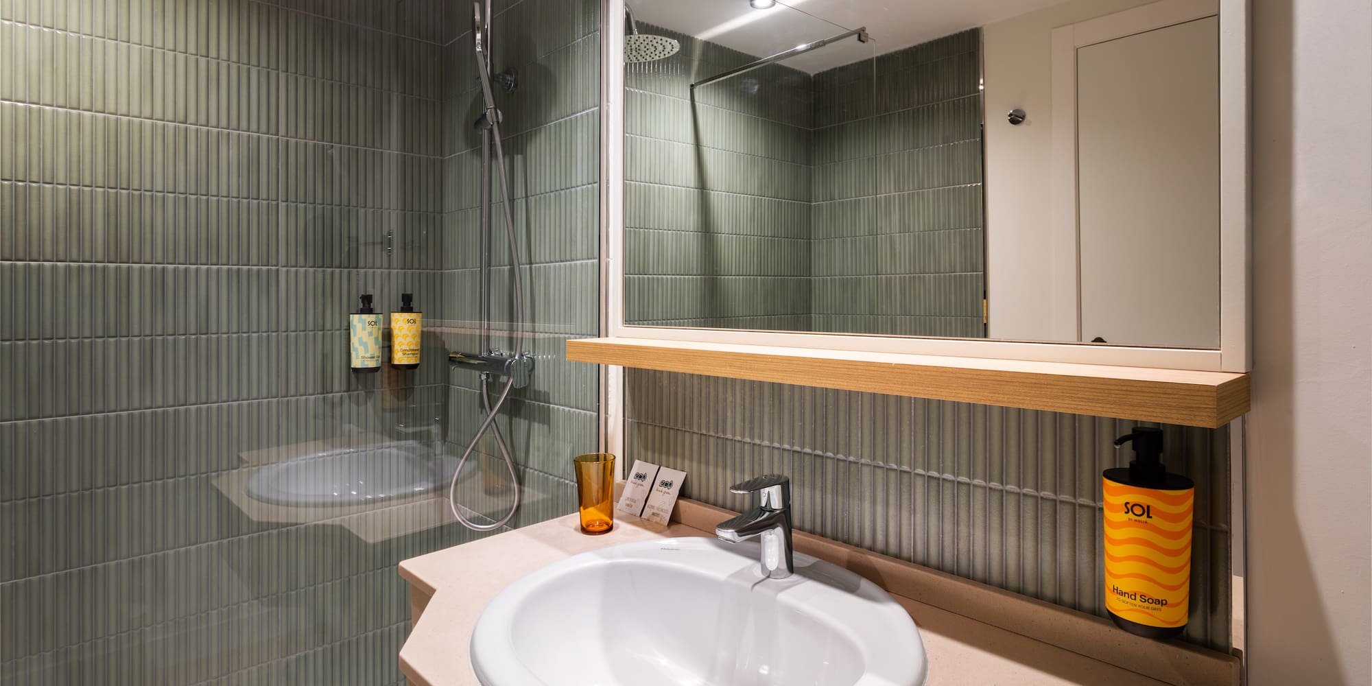 Modern hotel bathroom with green tiles, rainfall shower, and sleek sink.