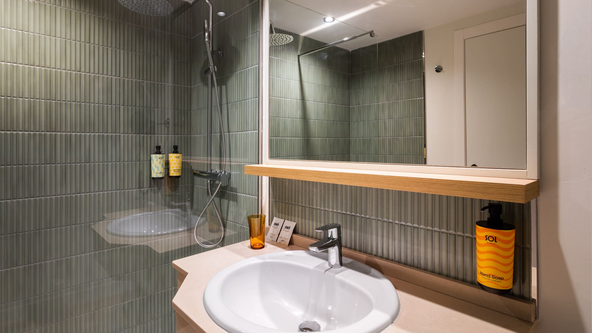 Modern hotel bathroom with green ribbed shower tiles, white sink, and mirror.