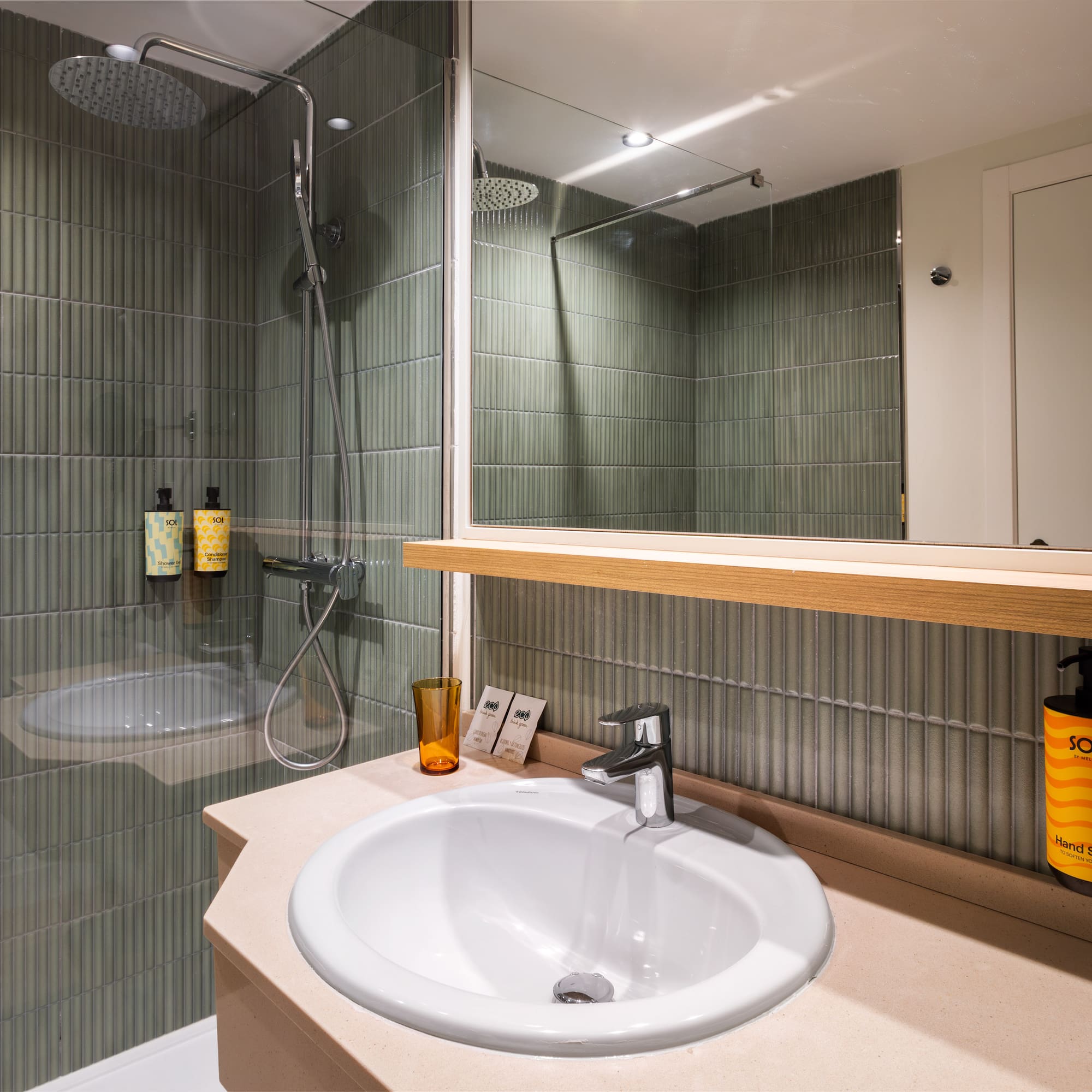 Modern hotel bathroom with green tiles, rainfall shower, and sleek sink.