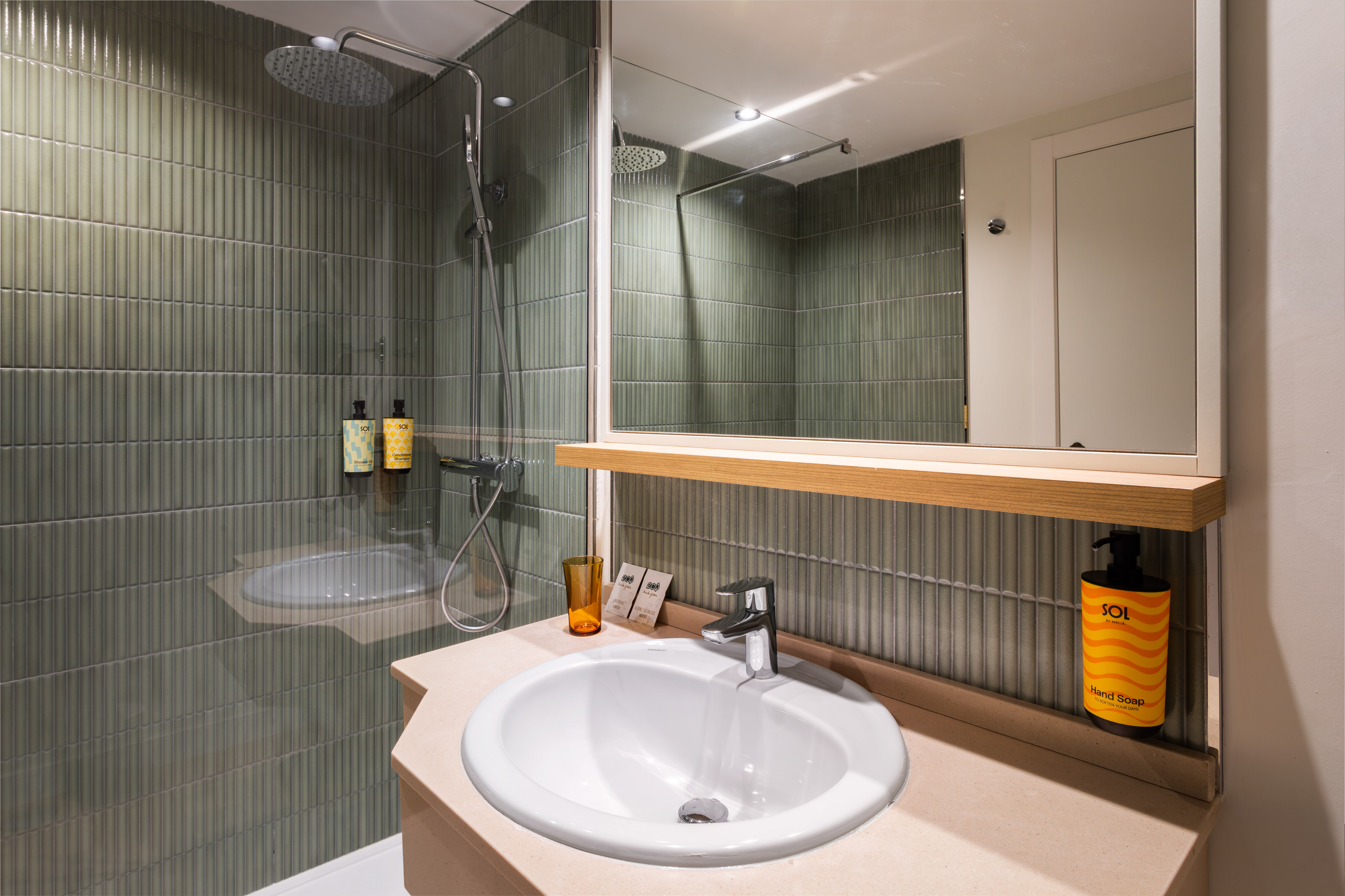 Modern hotel bathroom with green ribbed shower tiles, white sink, and mirror.