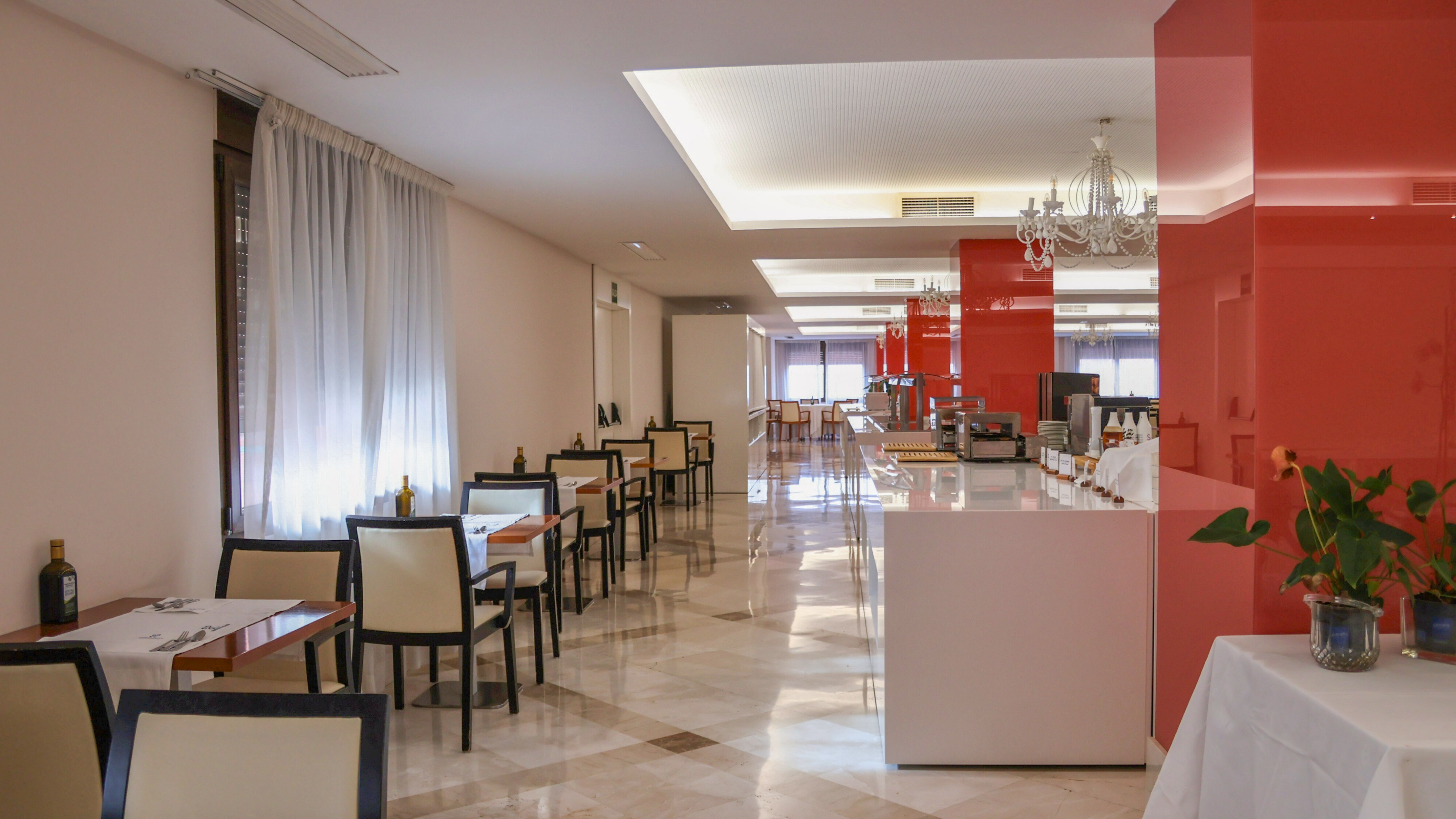 Modern hotel breakfast room with buffet, dining tables, and red accents.