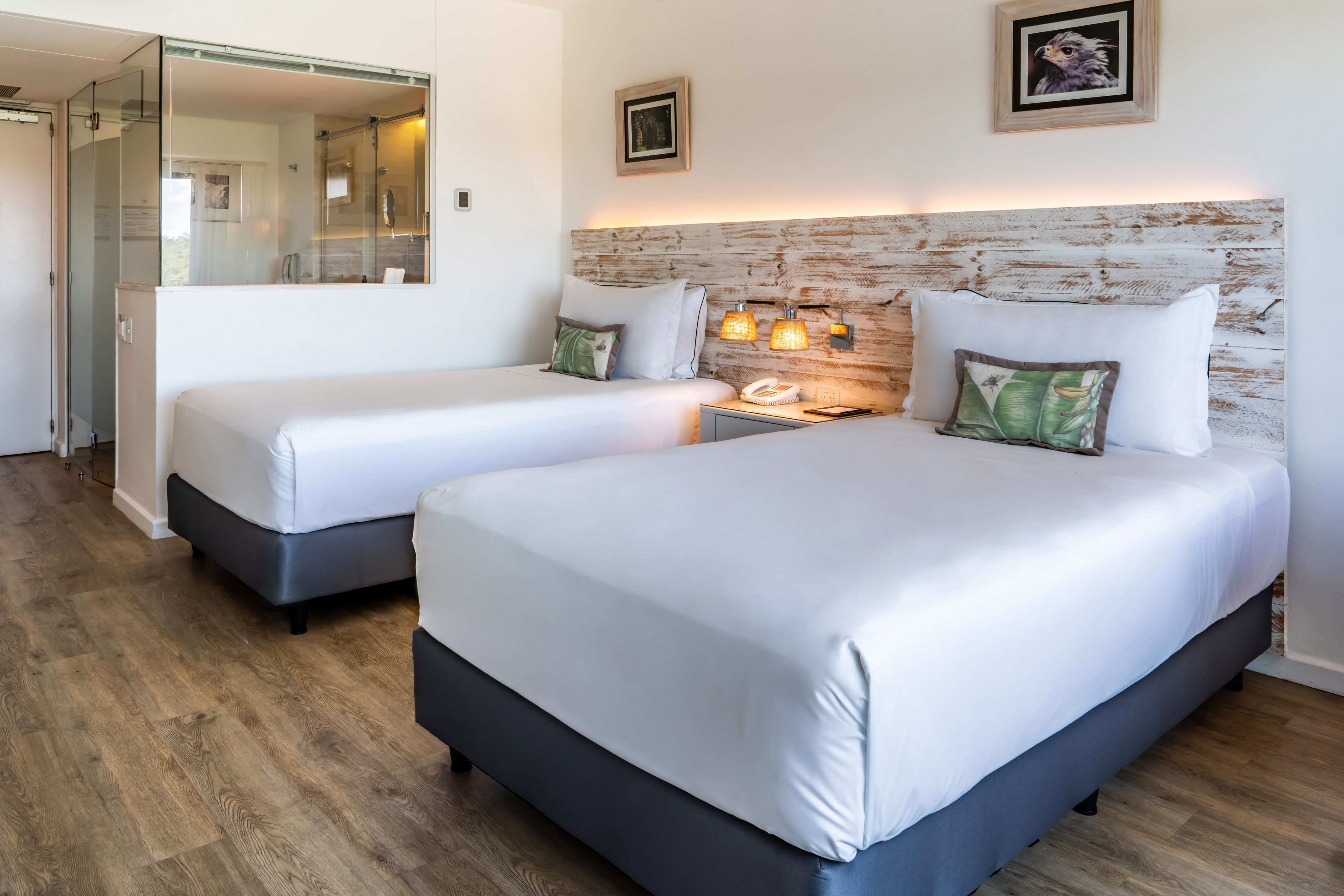 Modern hotel twin room with wooden headboard and glass bathroom partition.