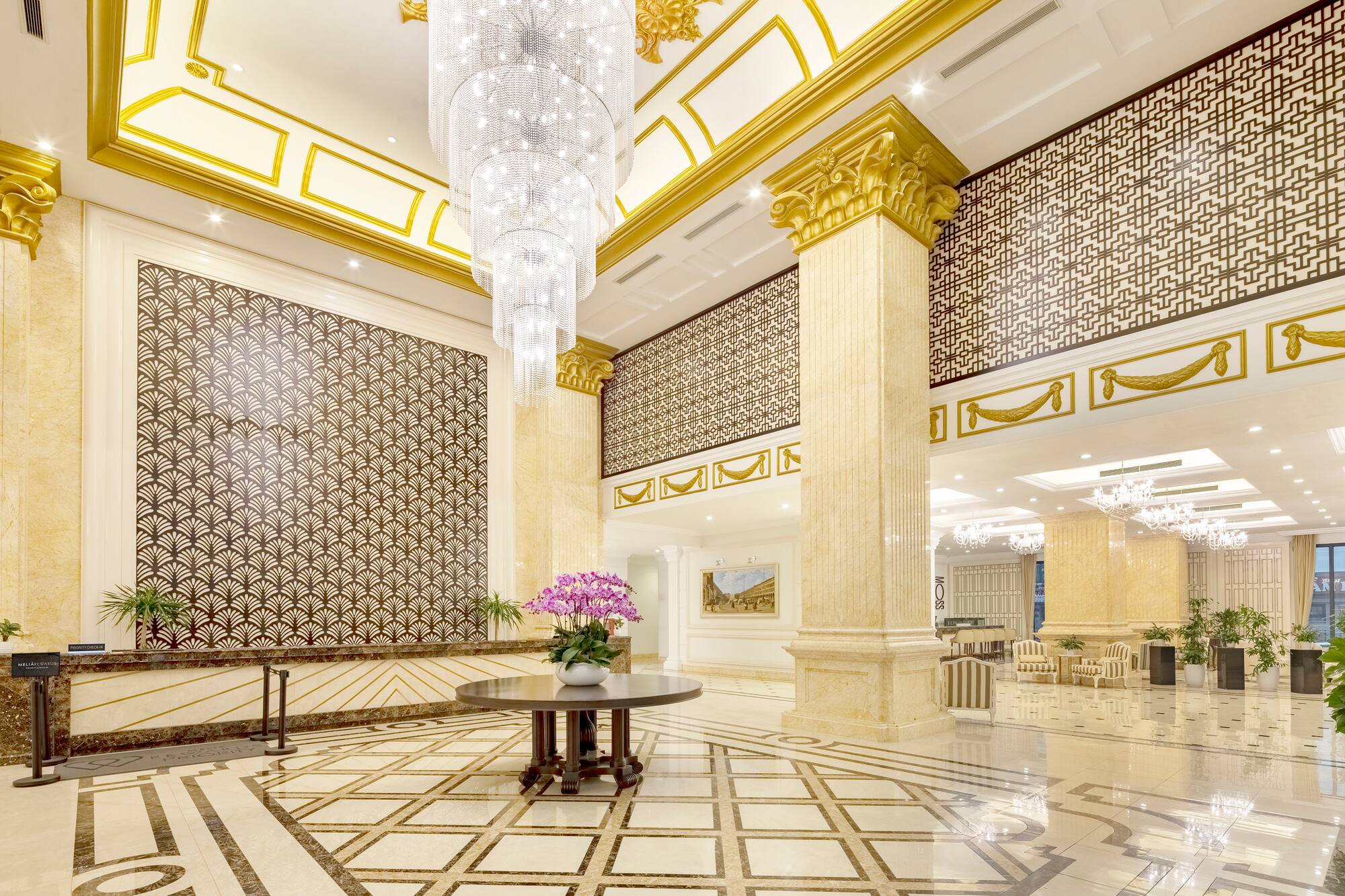 Luxurious hotel lobby with grand crystal chandelier, gold accents, and patterned marble floor.