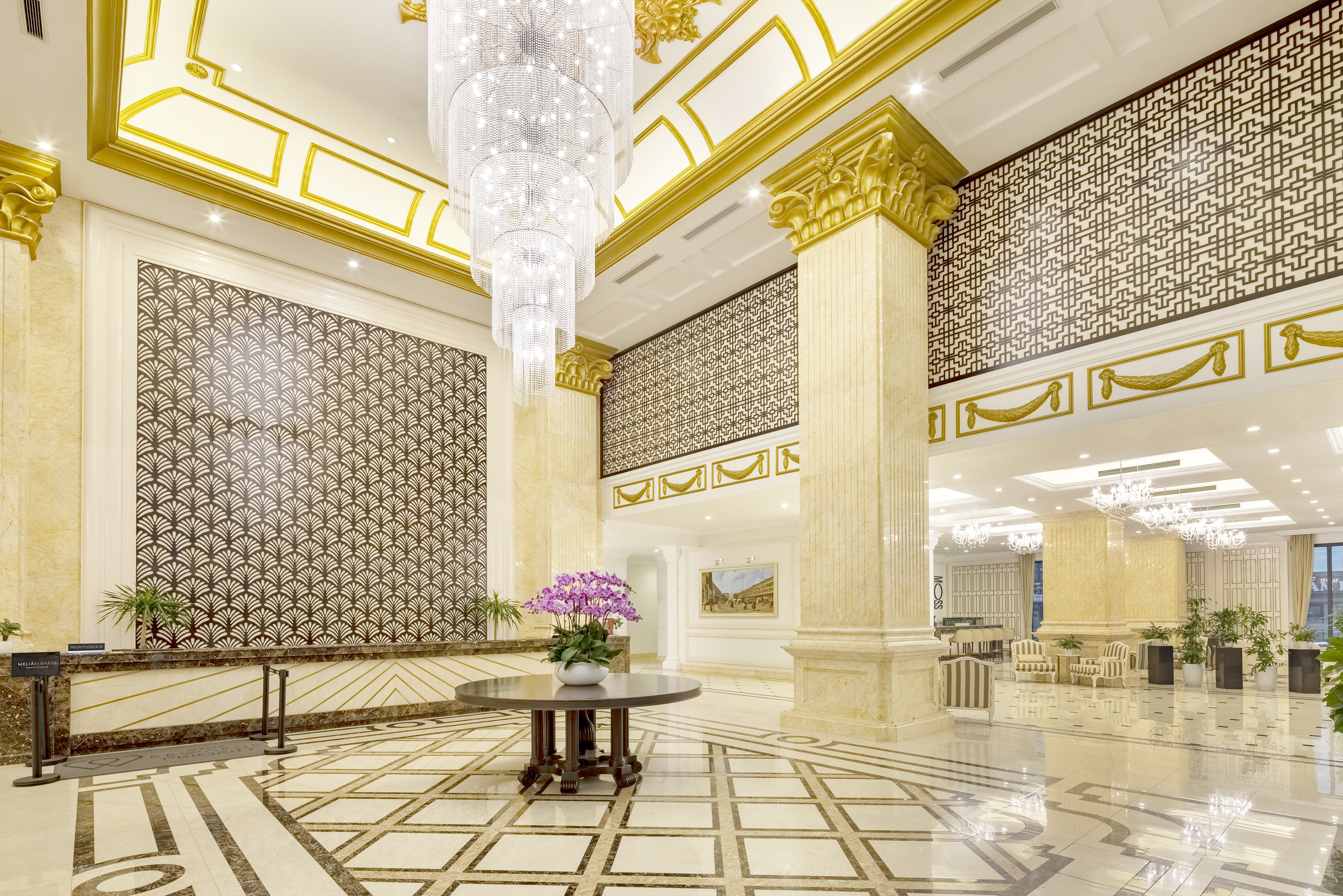 Luxurious hotel lobby with grand crystal chandelier, gold accents, and patterned marble floor.