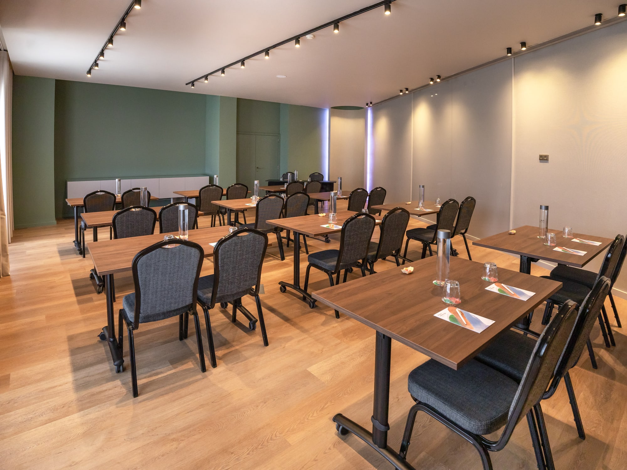 Modern meeting room, classroom setup, wood tables, dark chairs, green wall.