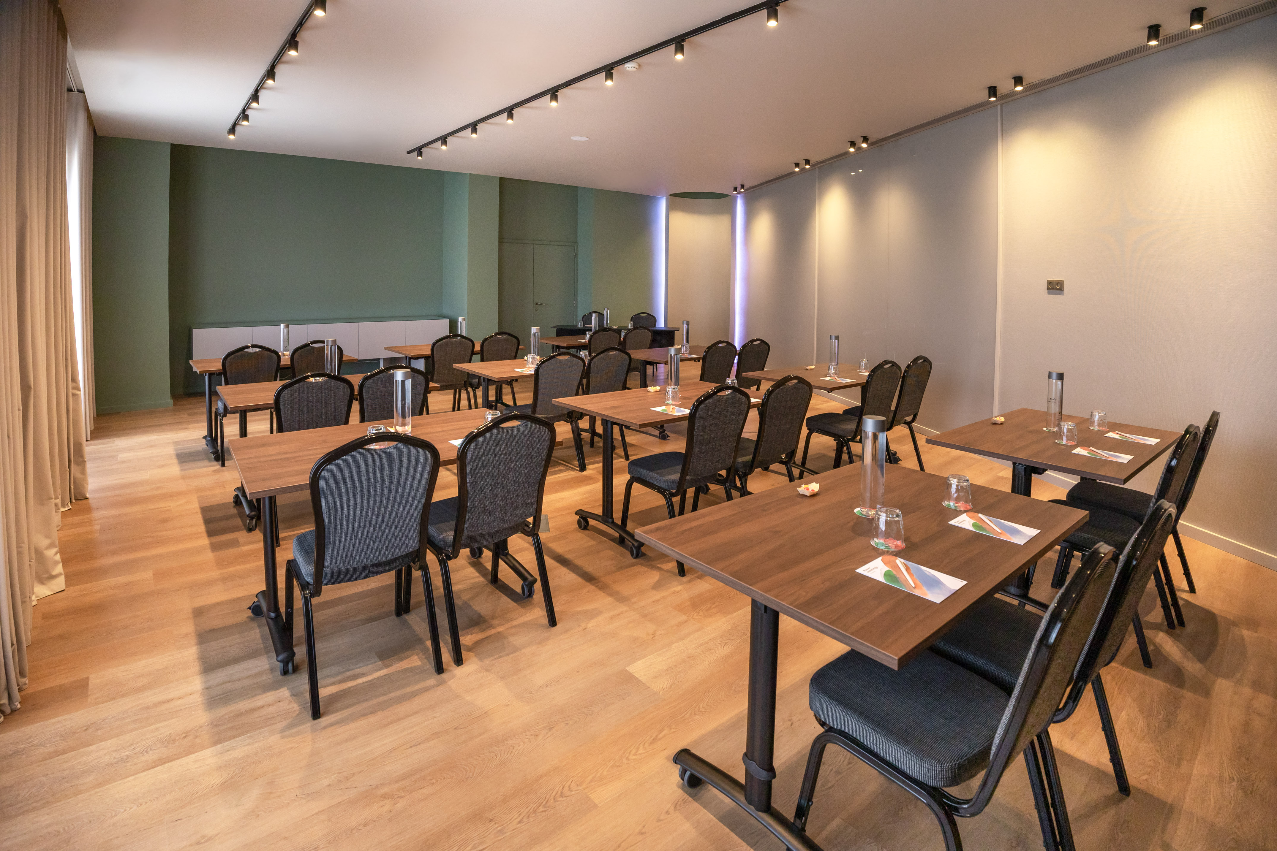 Modern meeting room, classroom setup, wood tables, dark chairs, green wall.