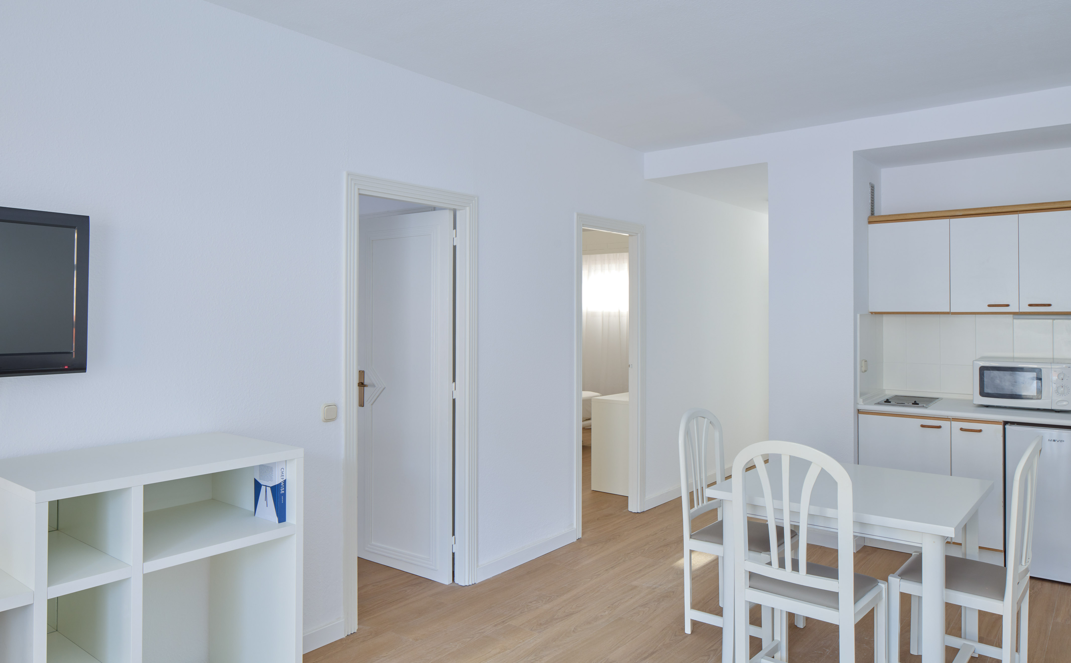 Bright white studio apartment with kitchenette, dining table, and living space.