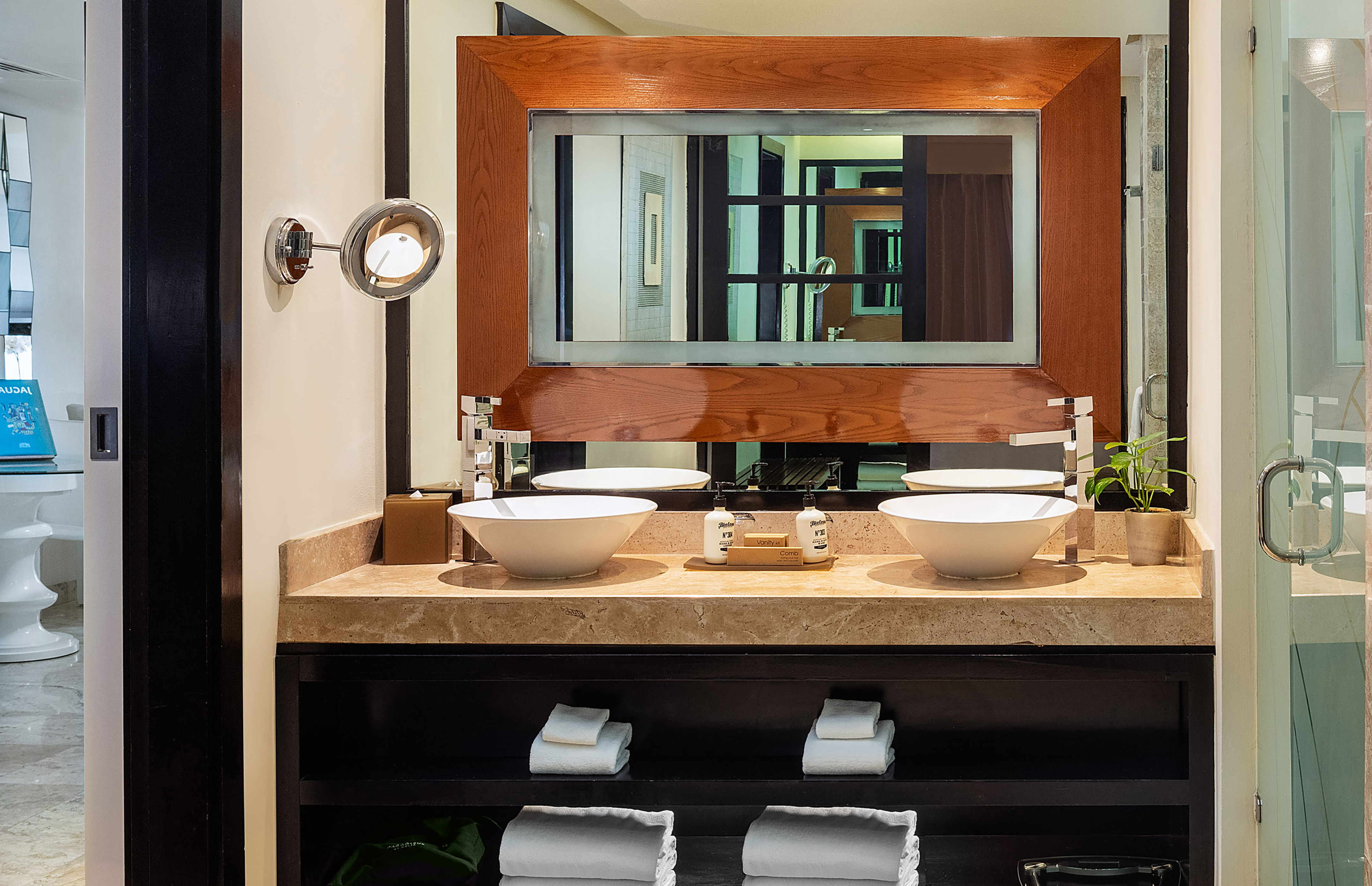 Hotel bathroom double vanity with white sinks, marble counter, wooden mirror.