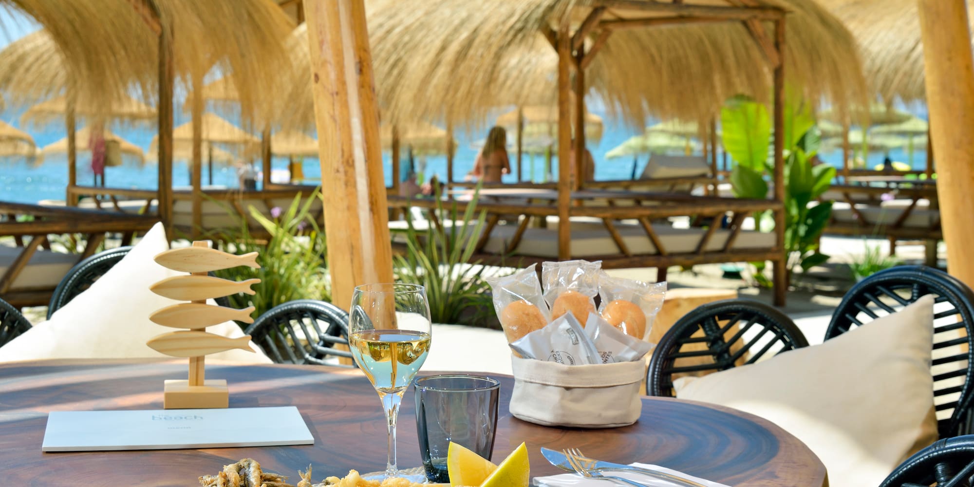 Fried seafood and wine on a beach restaurant table with thatched cabanas.