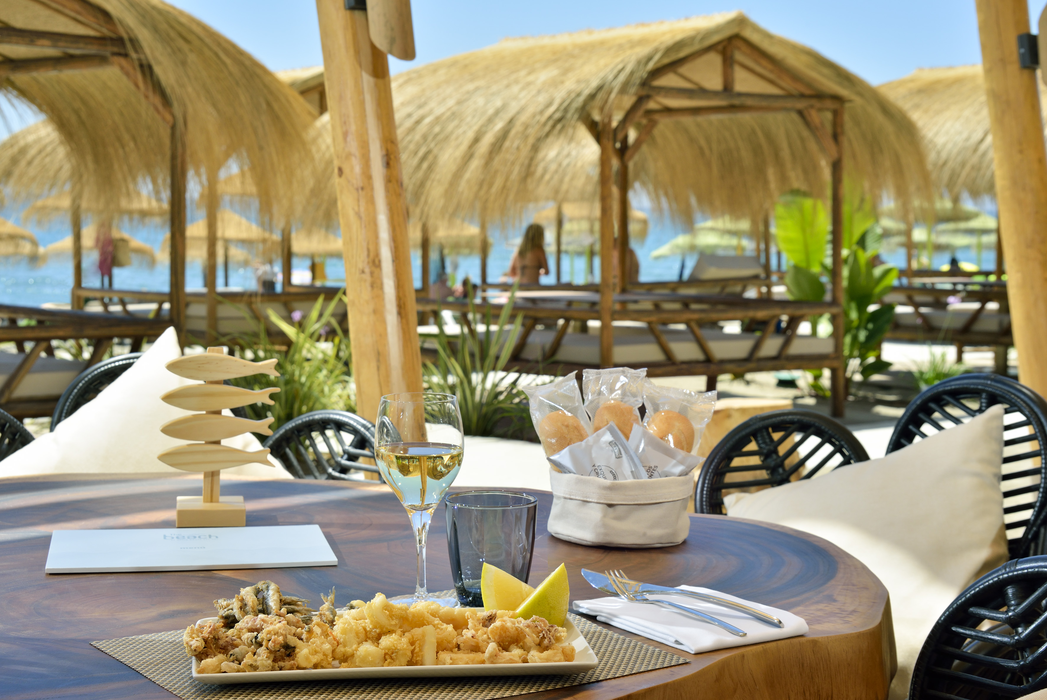 Fried seafood and wine on a beach restaurant table with thatched cabanas.