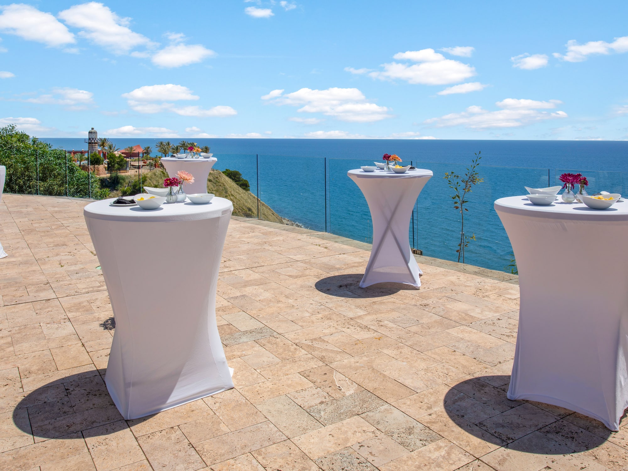 White cocktail tables on a sunny oceanfront patio for an outdoor event.