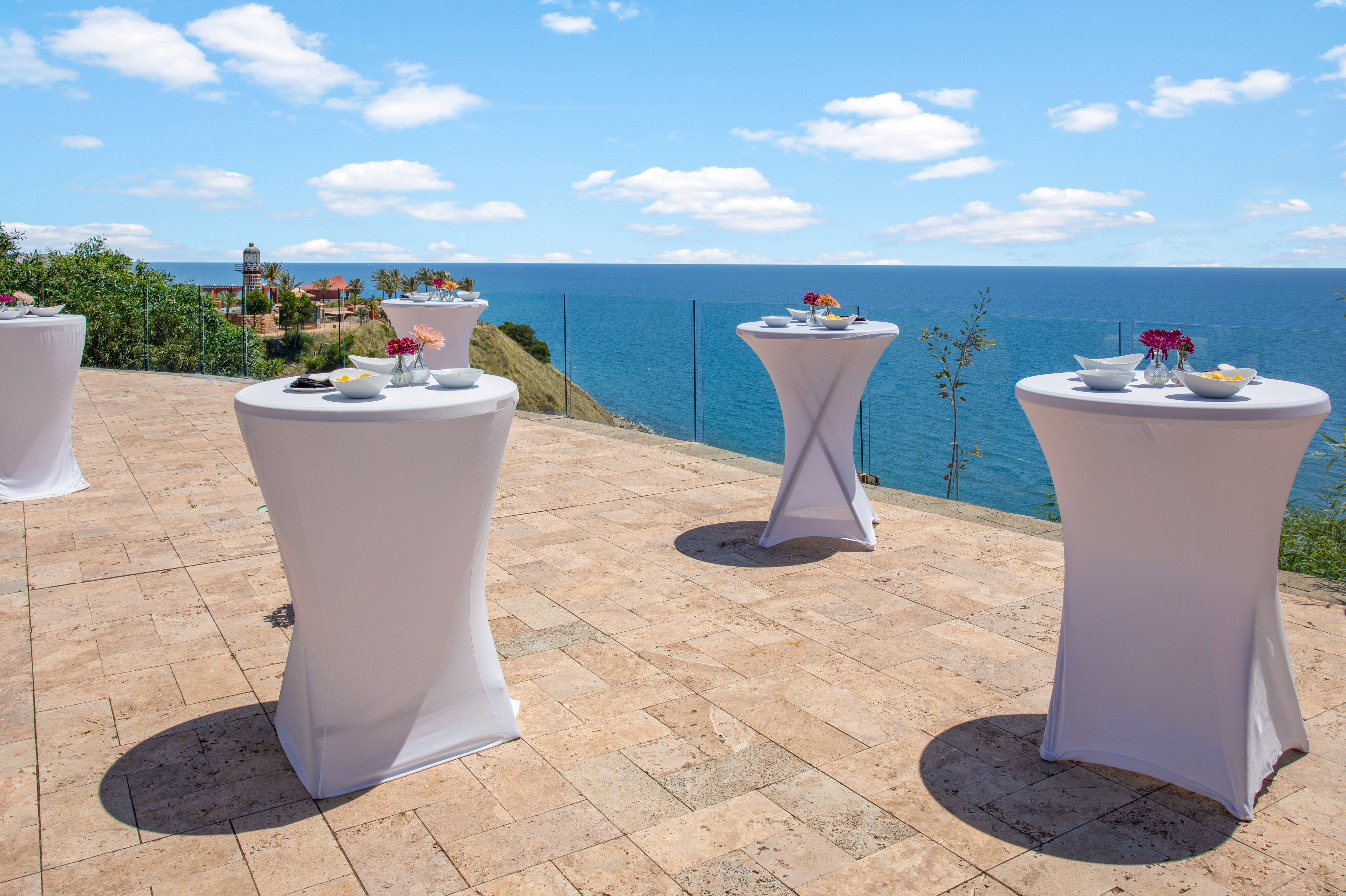 White cocktail tables on a sunny oceanfront patio for an outdoor event.