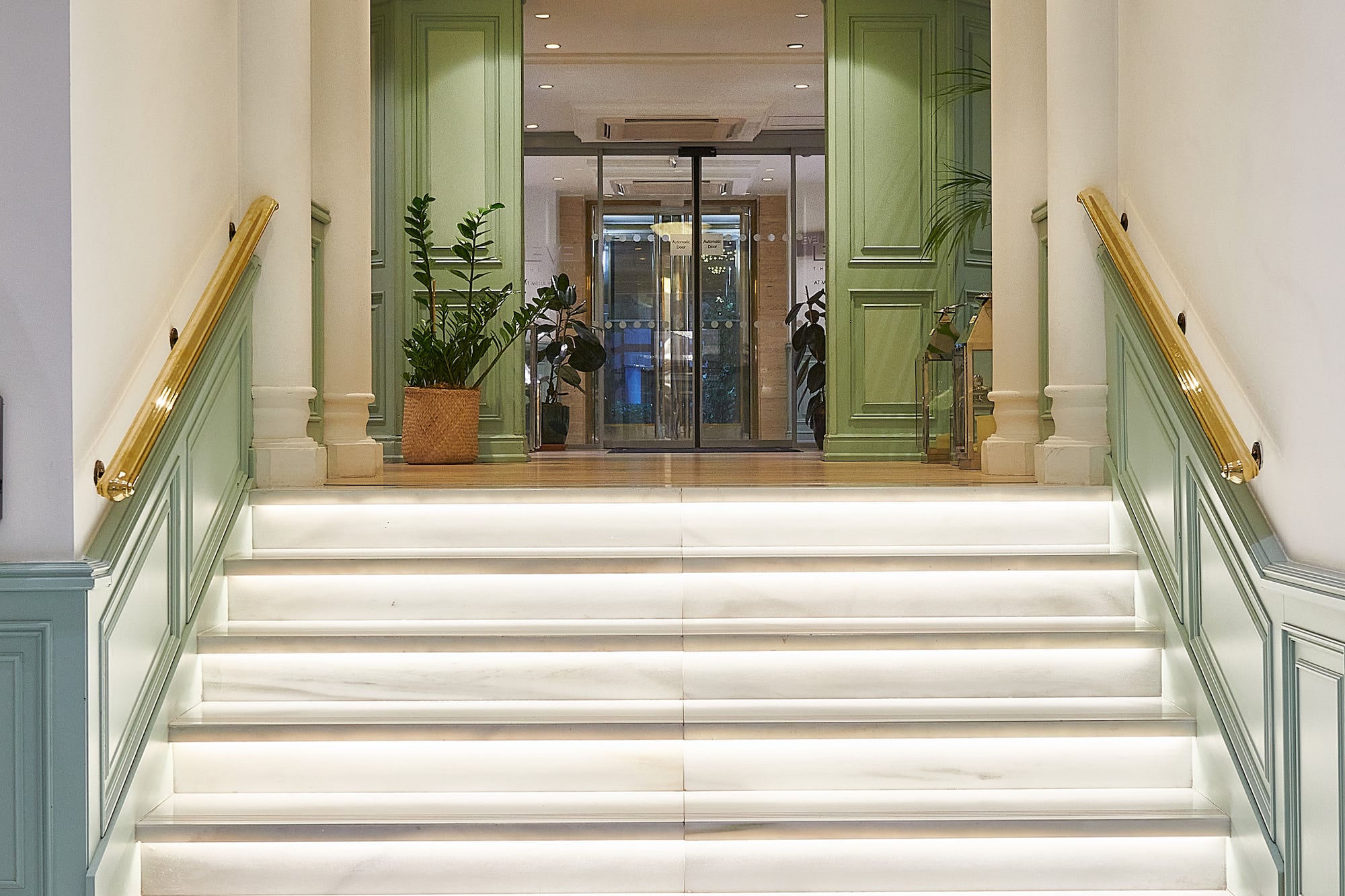 Illuminated marble staircase with gold handrails in a hotel lobby entrance.