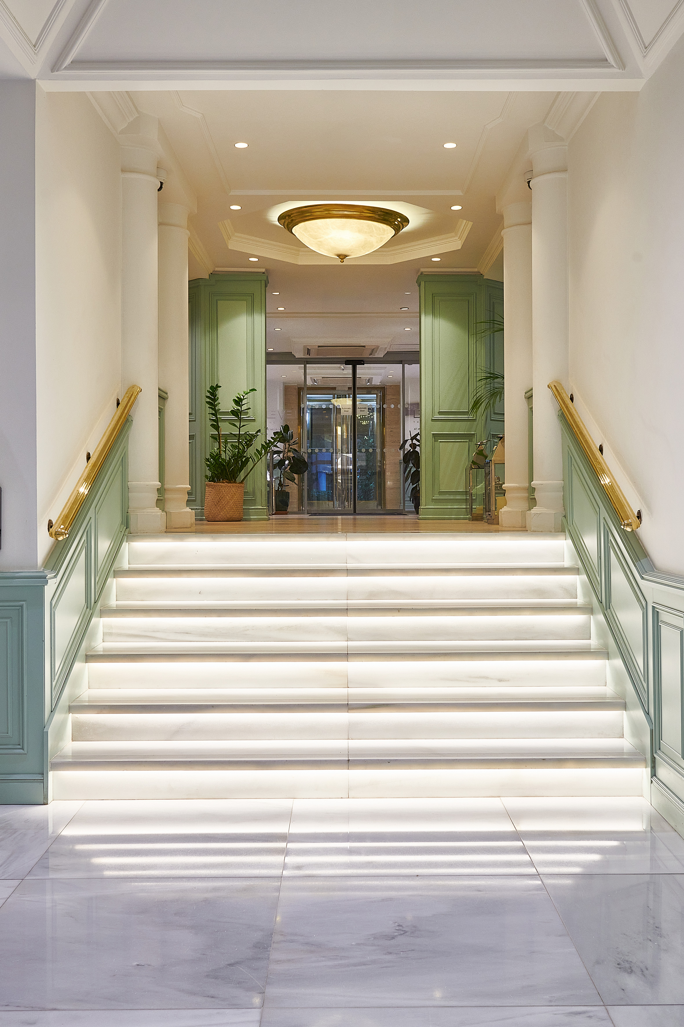 Illuminated marble staircase with gold handrails in a hotel lobby entrance.