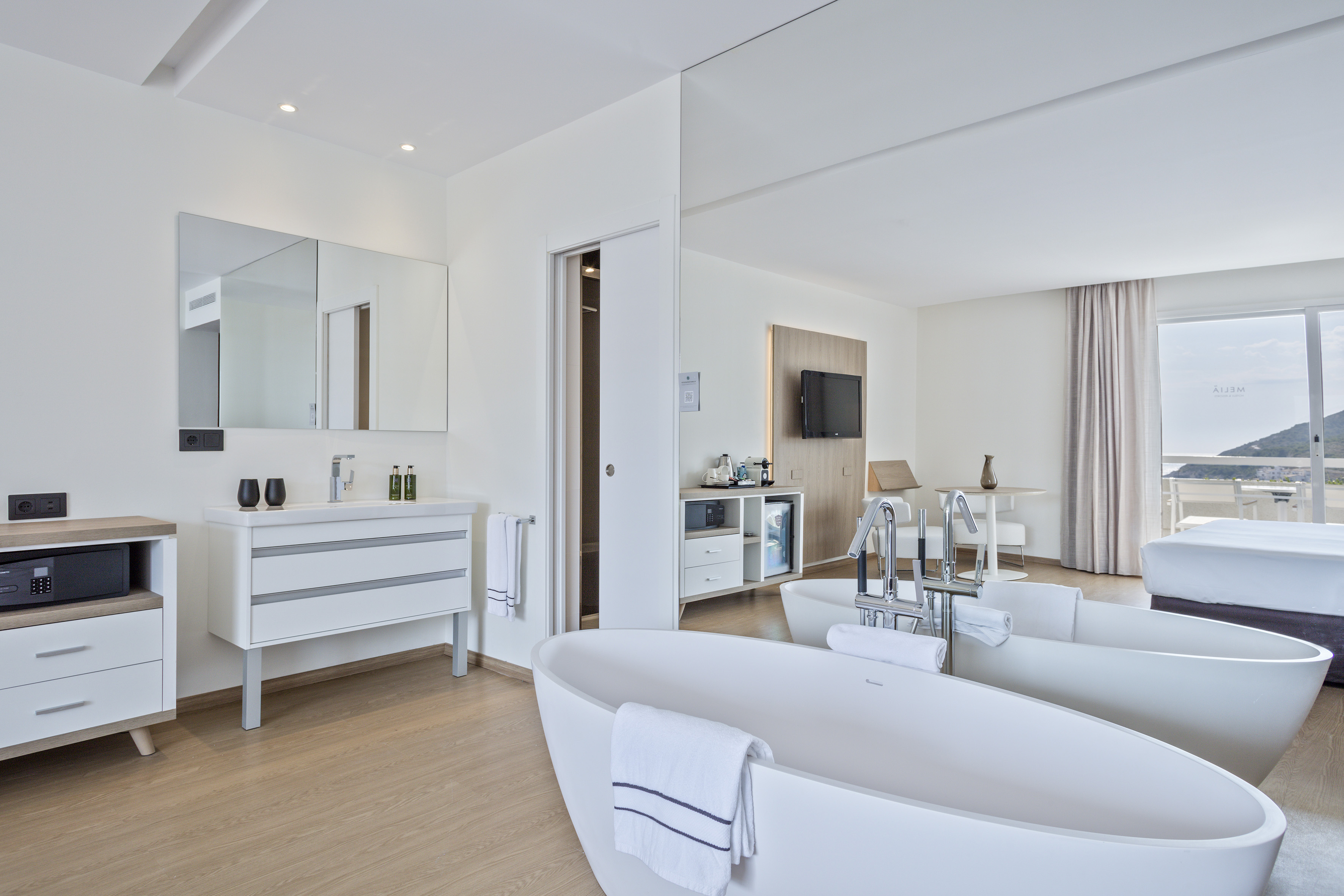 Luxury hotel suite with open-plan bathroom, twin bathtubs, and balcony view.
