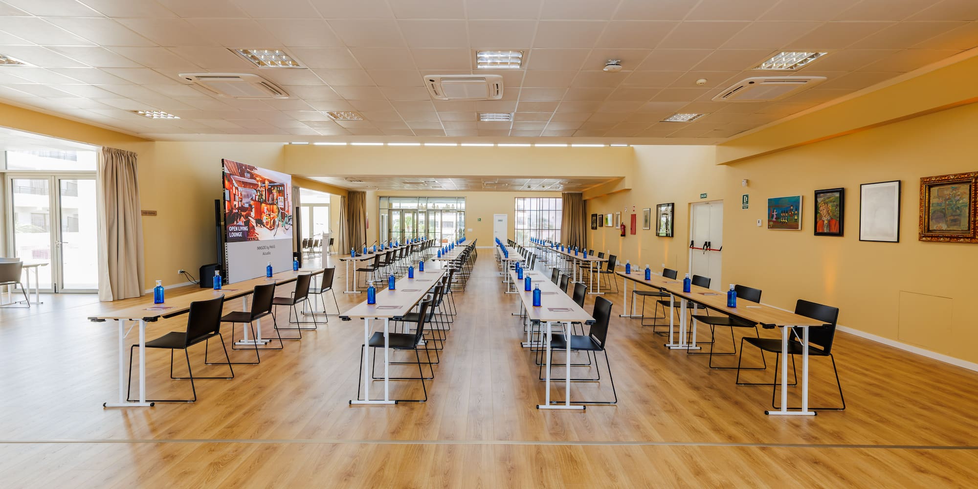 Empty conference room with tables, chairs, water bottles, and large screen.