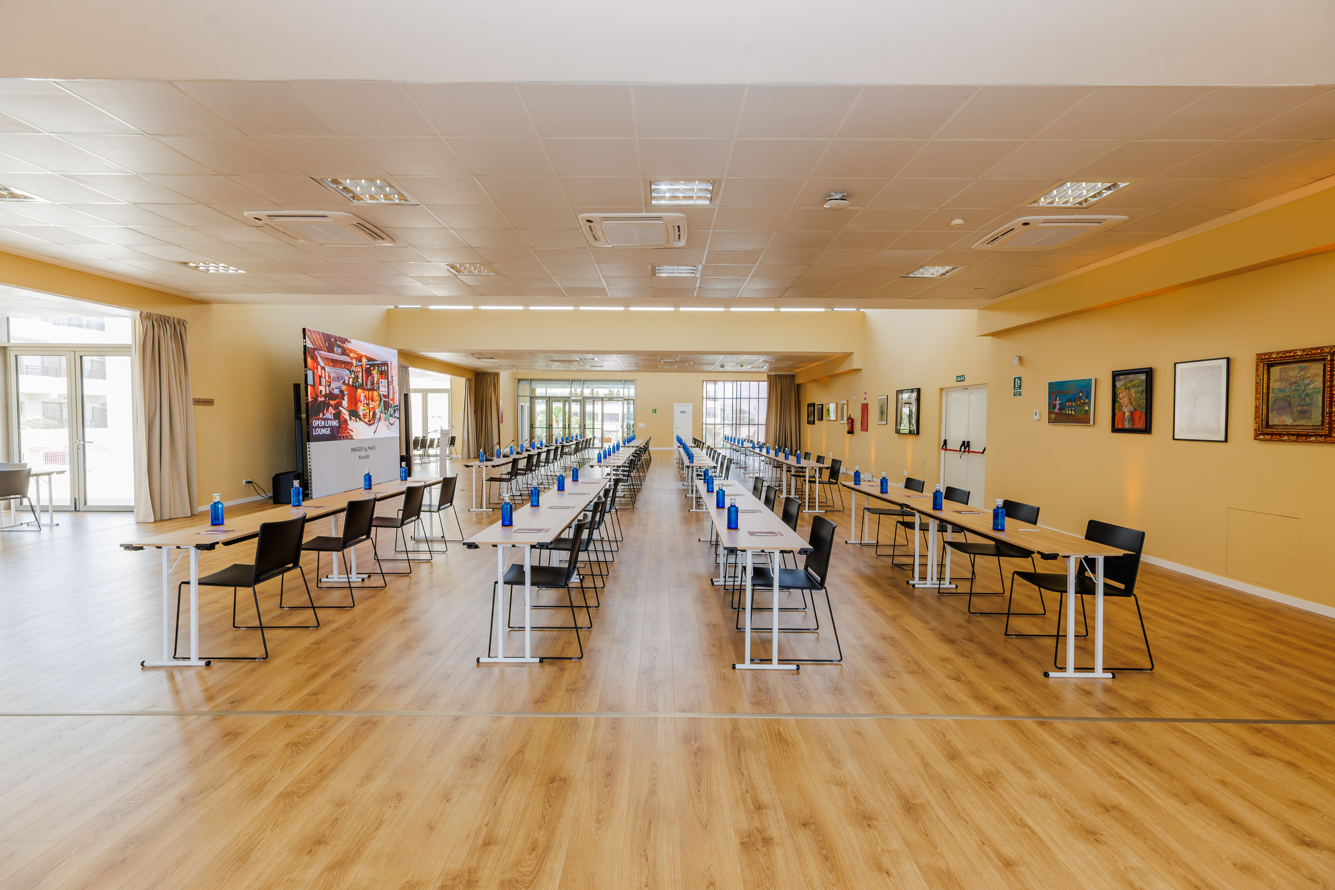 Empty conference room with tables, chairs, water bottles, and large screen.