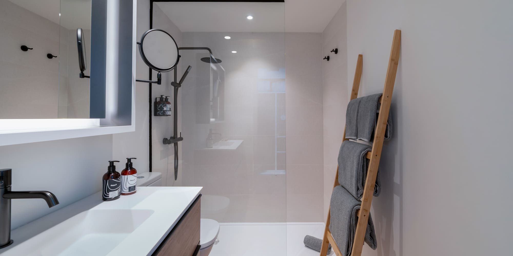 Baño moderno con ducha, lavabo, toallero de escalera y suelo de madera.