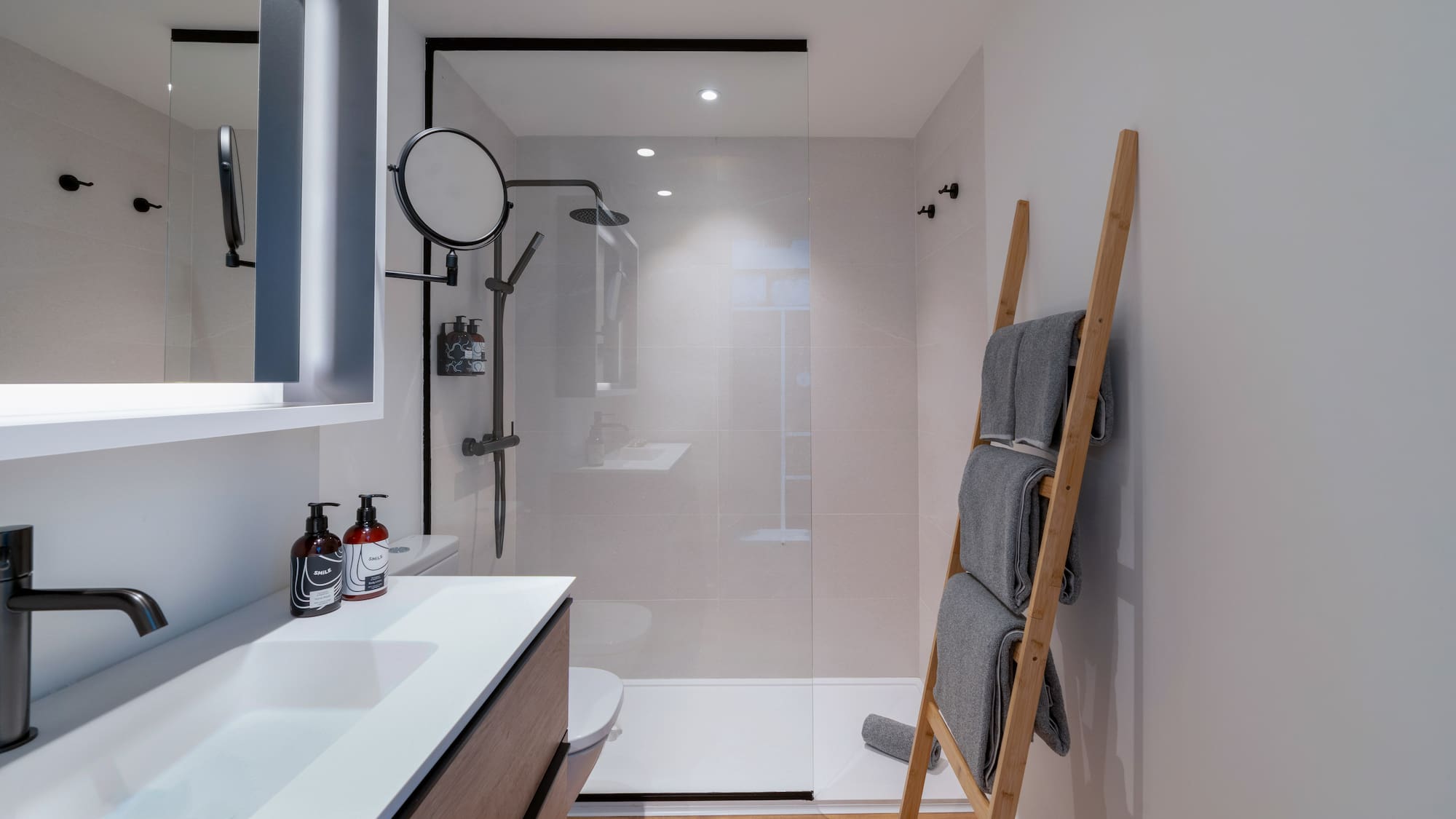 Baño moderno con ducha, lavabo, toallero de escalera y suelo de madera.