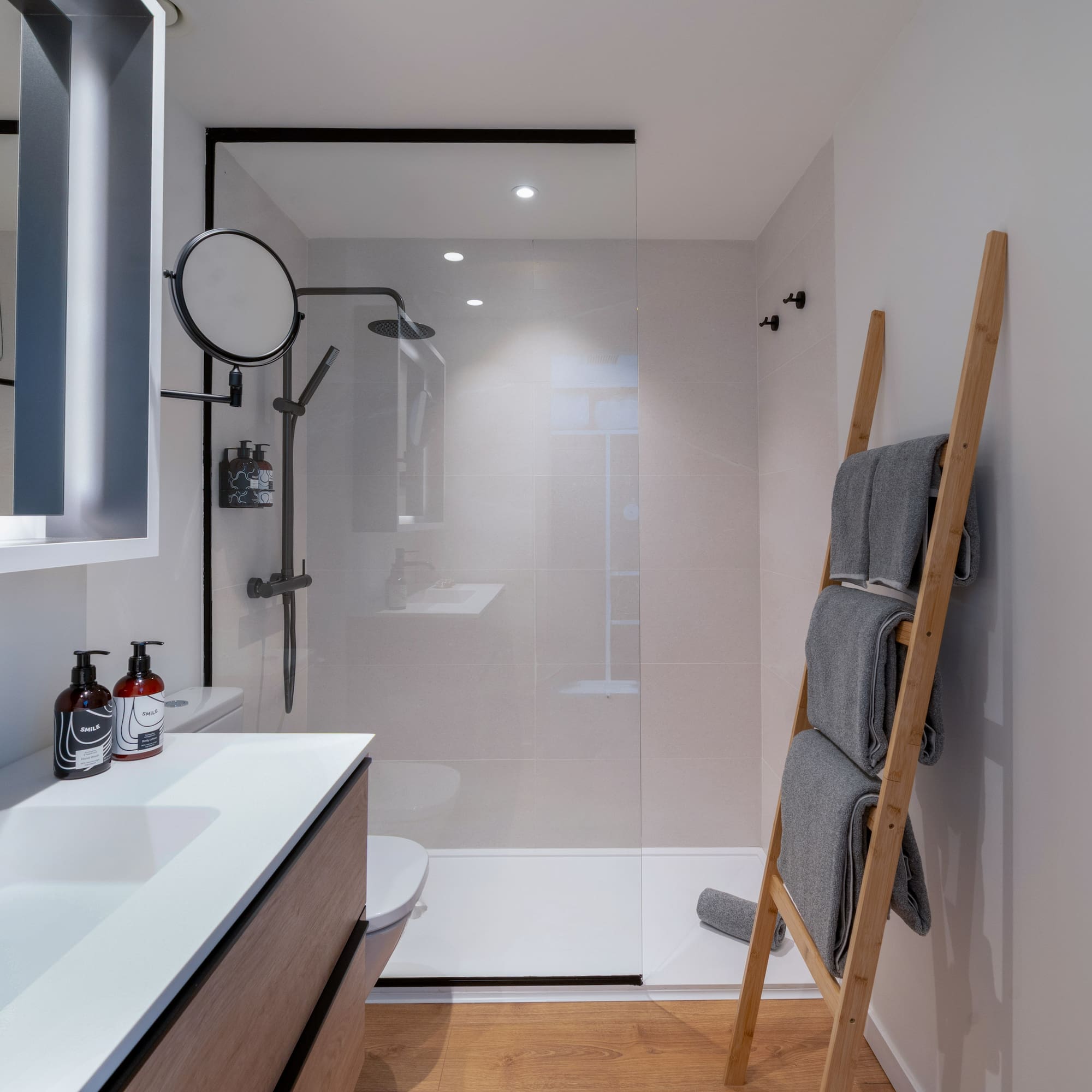 Baño moderno con ducha, lavabo, toallero de escalera y suelo de madera.