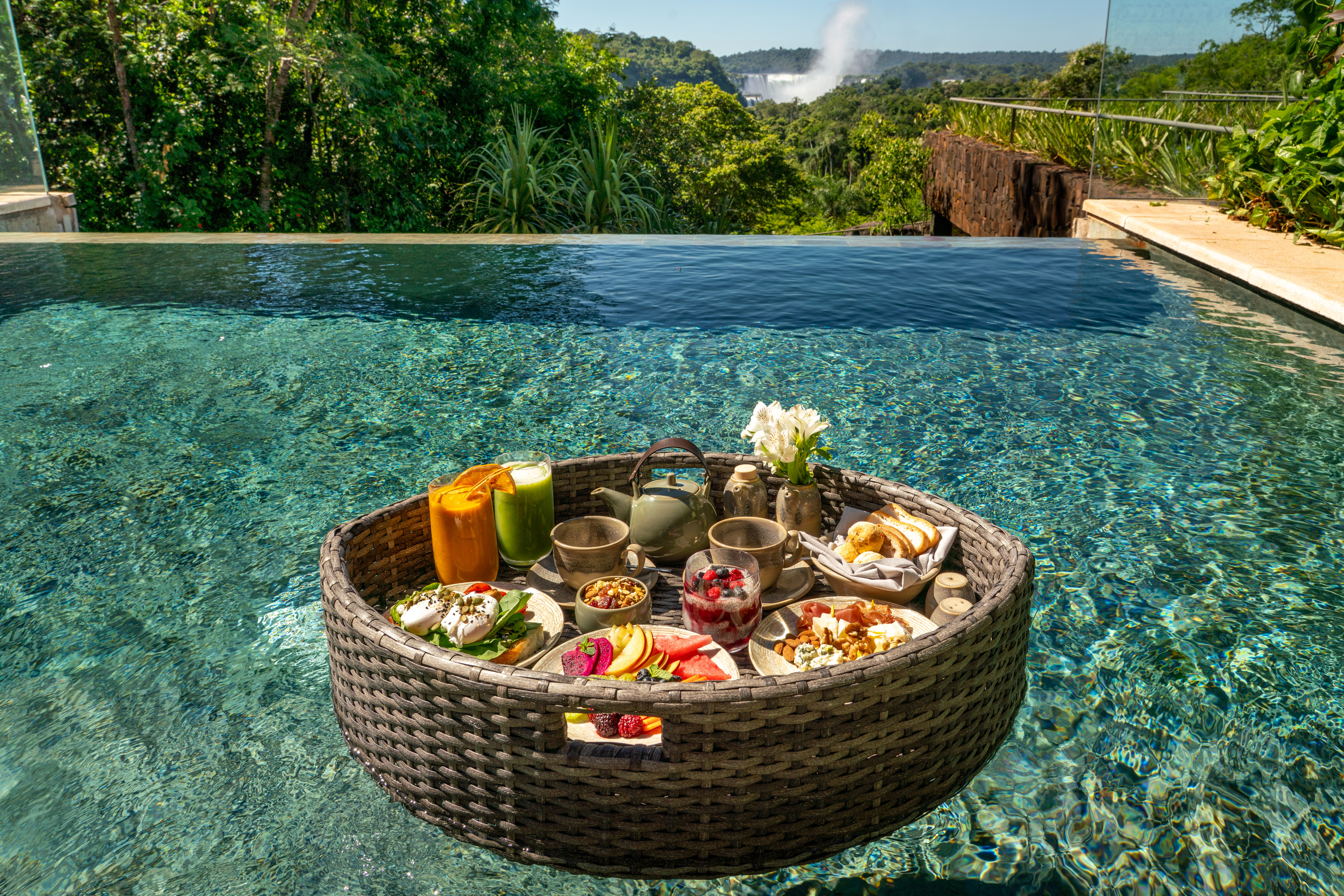 Floating breakfast in infinity pool overlooking Iguazu Falls and lush forest.