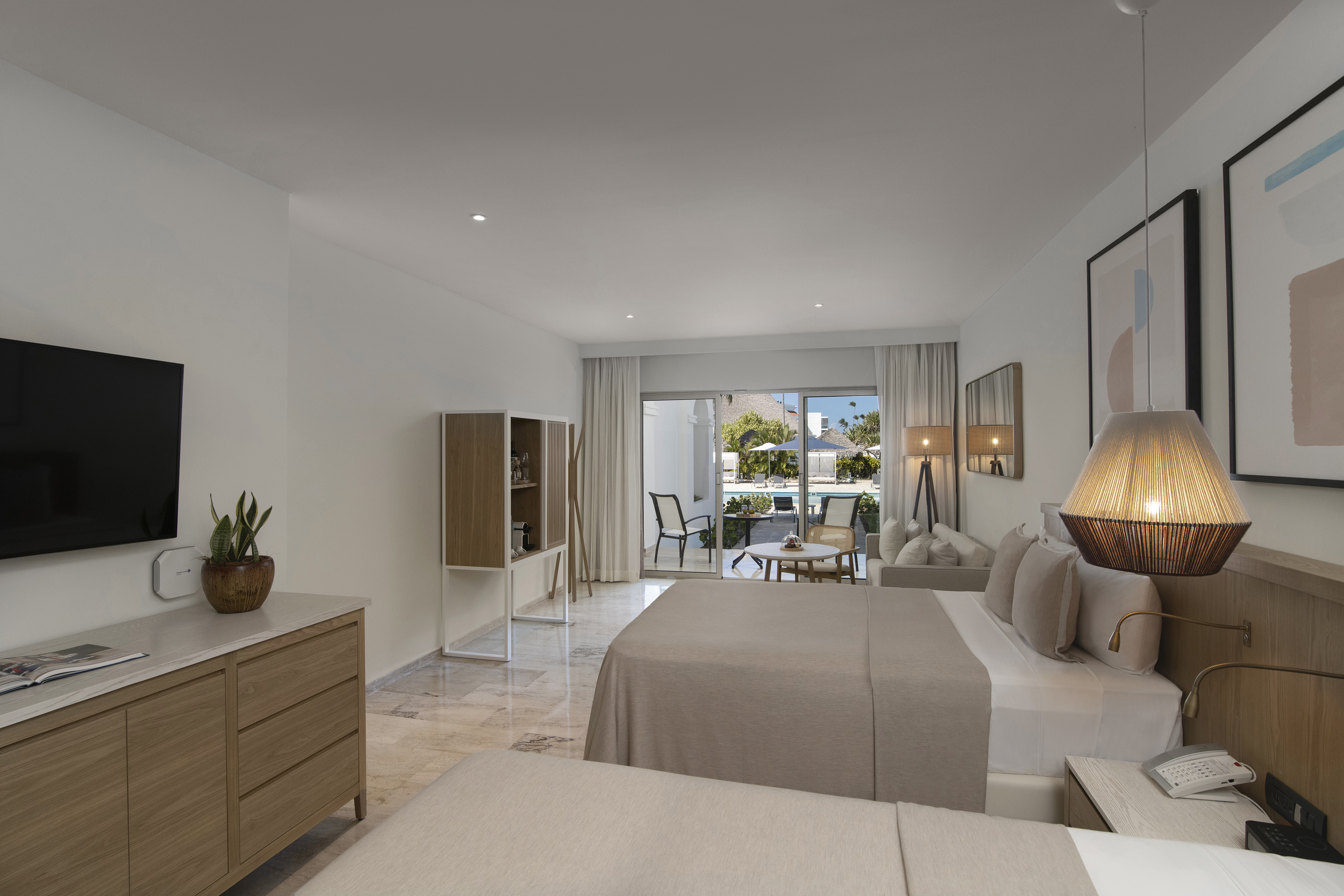 Modern hotel room with two beds, outdoor patio, and resort pool view.