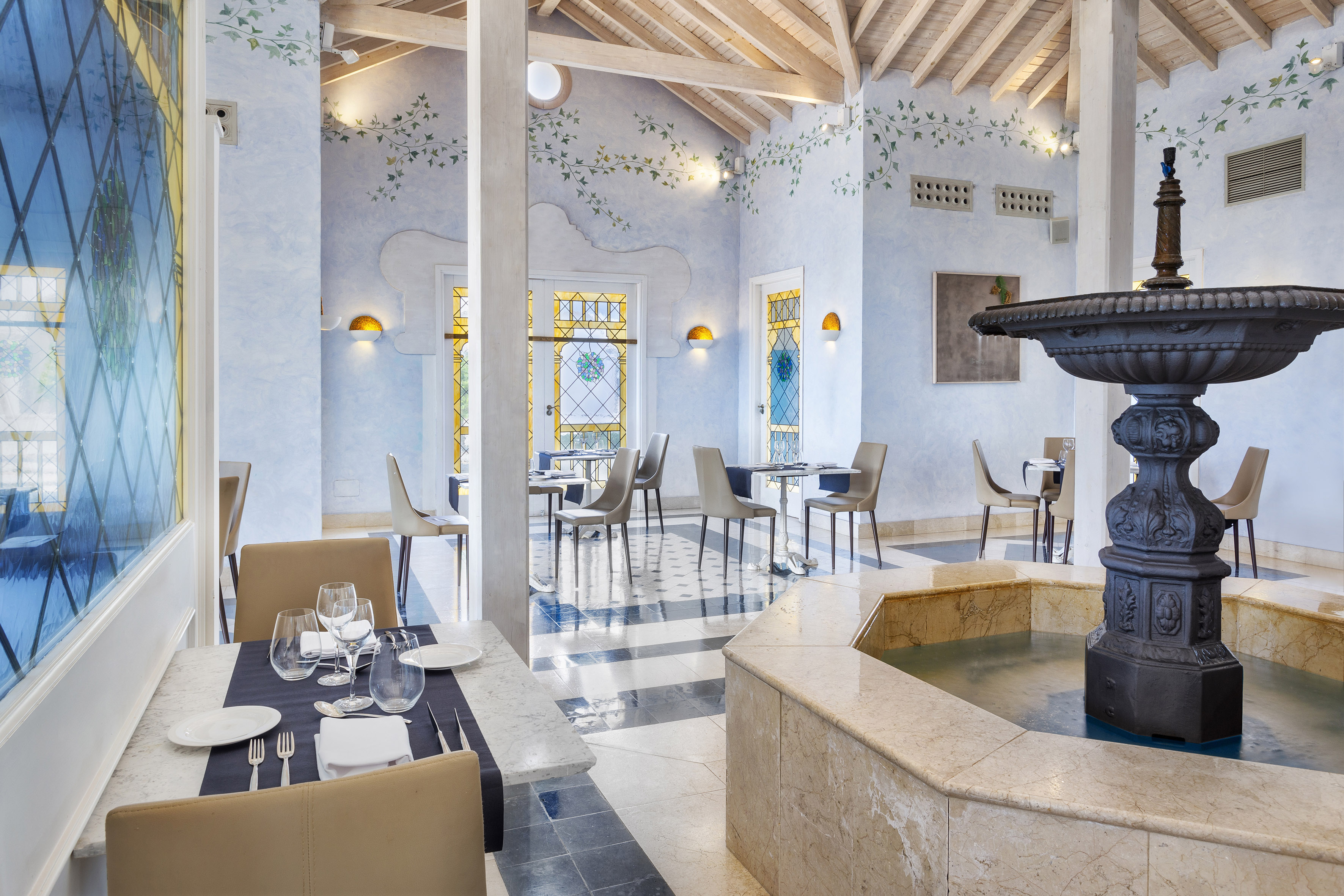 Restaurant dining room with vine murals, stained glass, and a large fountain.