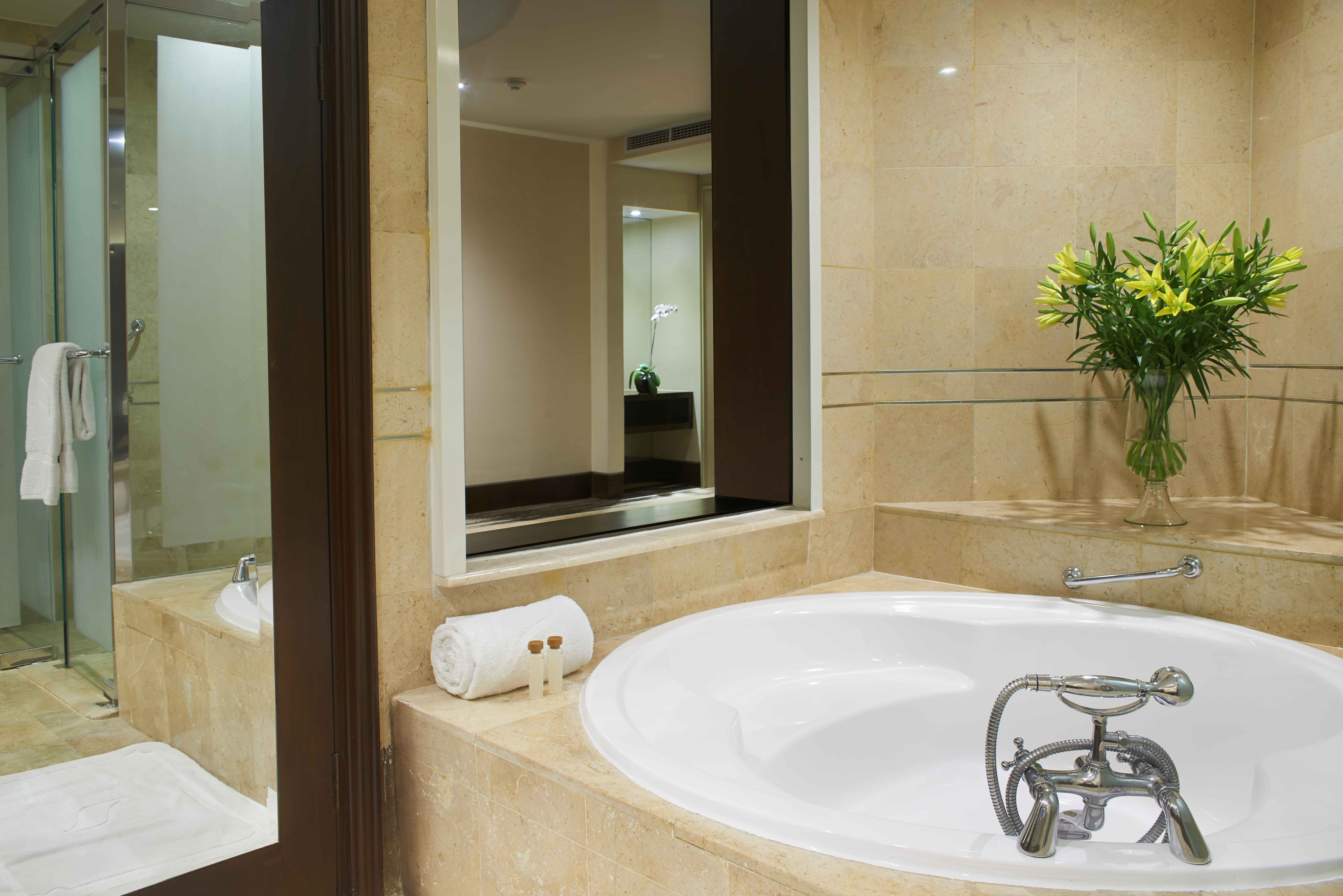 Luxury bathroom with large white bathtub, marble walls, and yellow lilies.