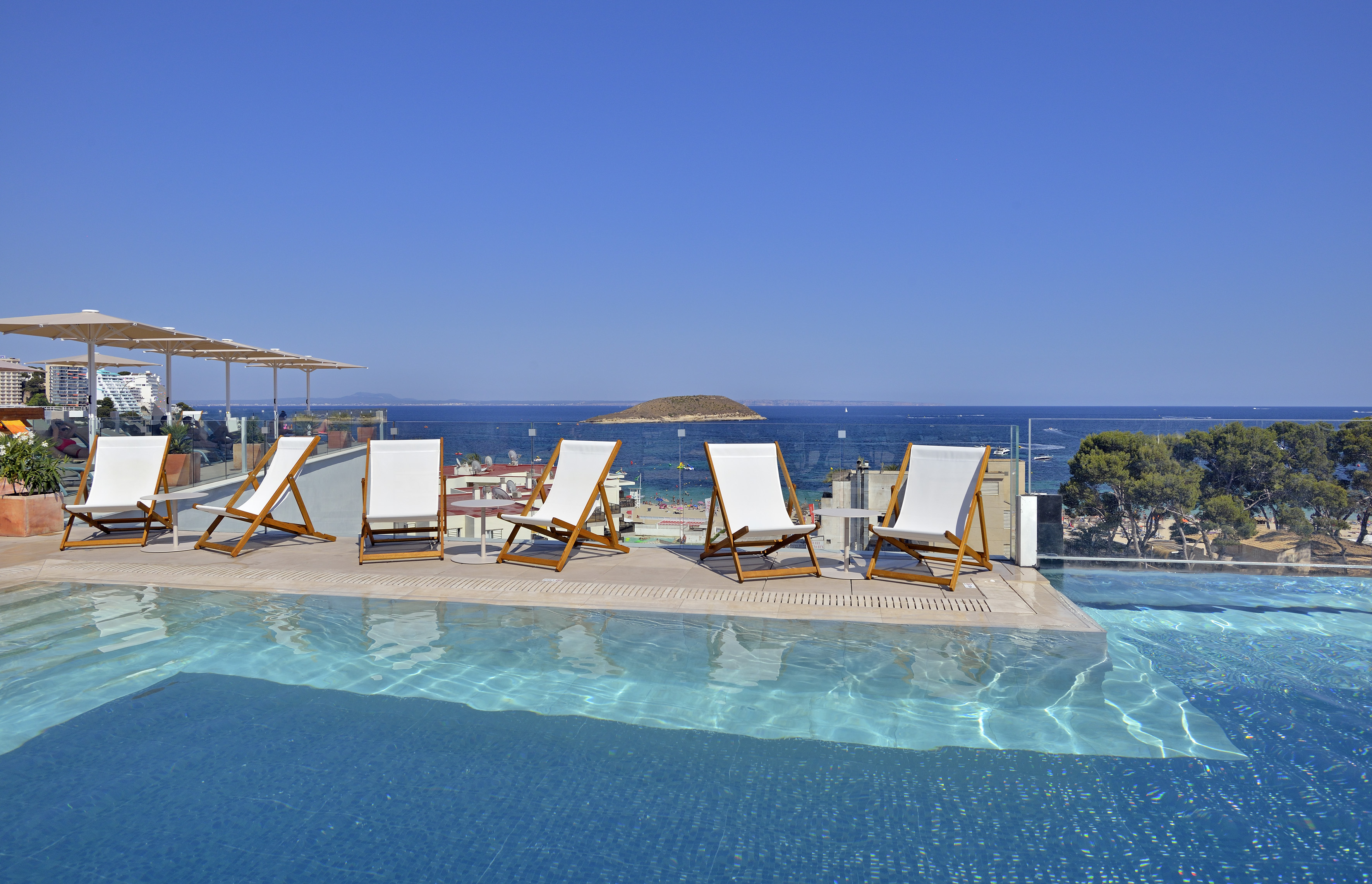 Rooftop infinity pool, lounge chairs, and ocean view on a sunny day.