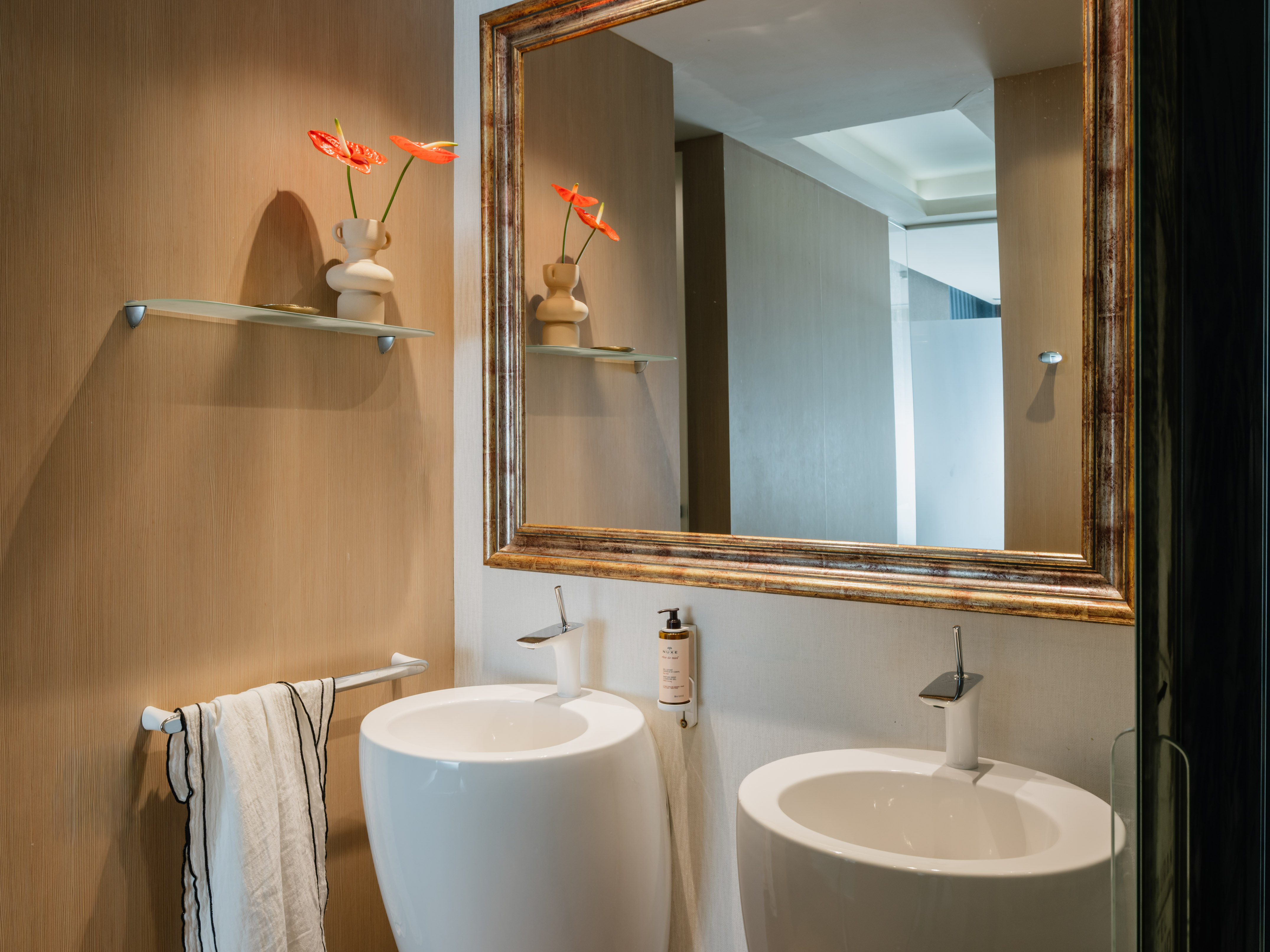 Modern bathroom with twin sinks, ornate mirror, wood wall, anthurium.