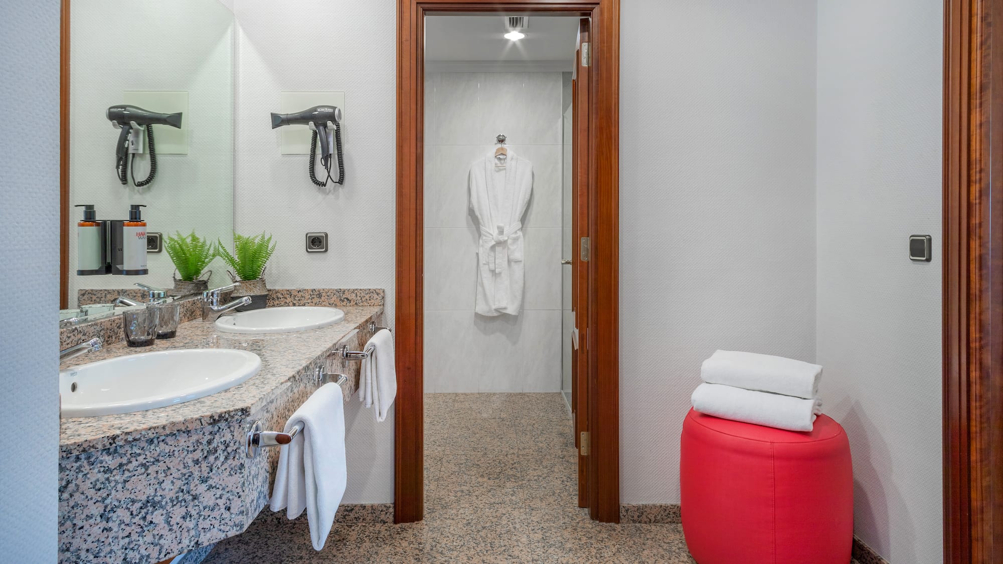 Double vanity hotel bathroom with granite countertop, bath amenities, and robe.