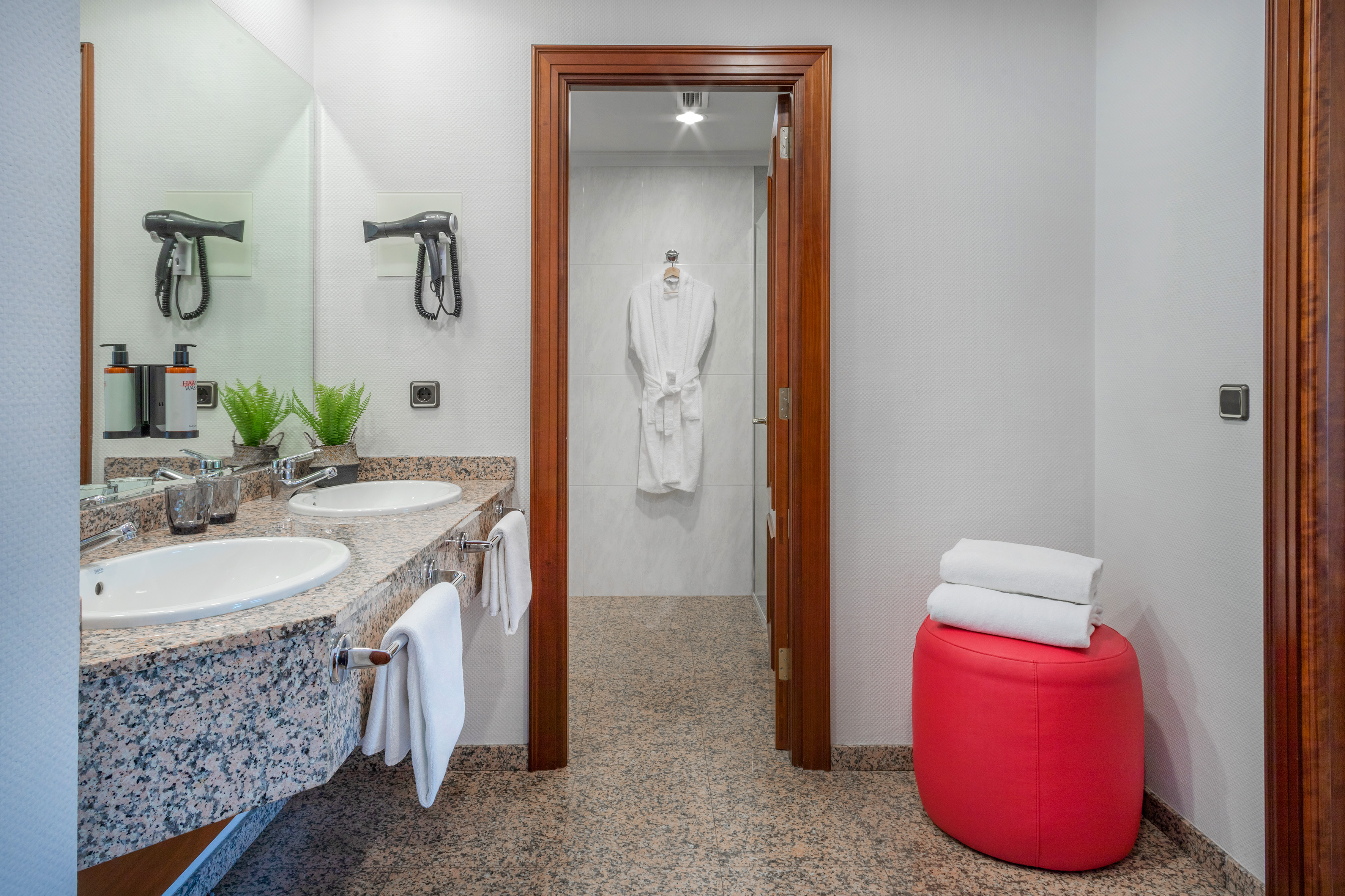 Double vanity hotel bathroom with granite countertop, bath amenities, and robe.