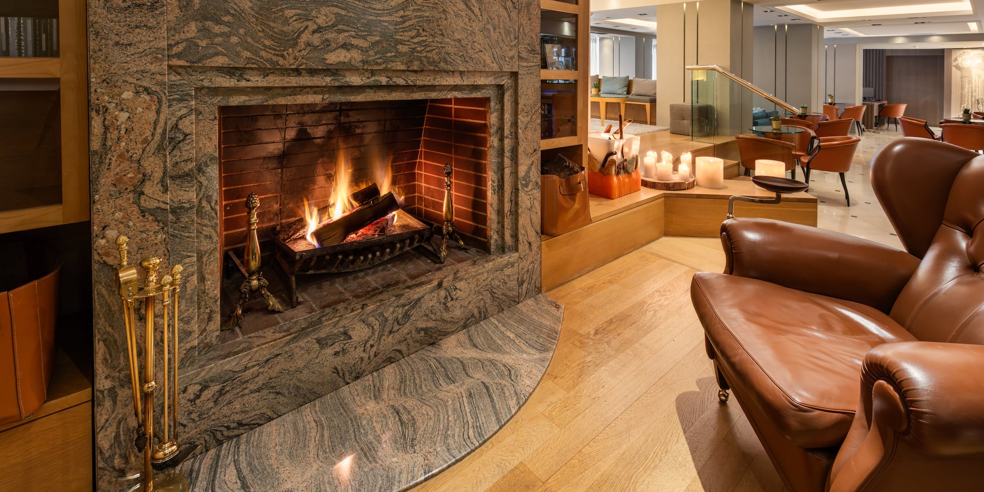 Warm hotel lounge with a marble fireplace, burning logs, and leather armchair.