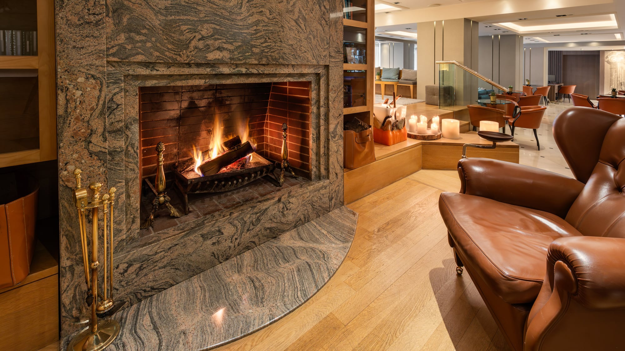 Hotel lounge with cozy granite fireplace, burning fire, and leather armchair.