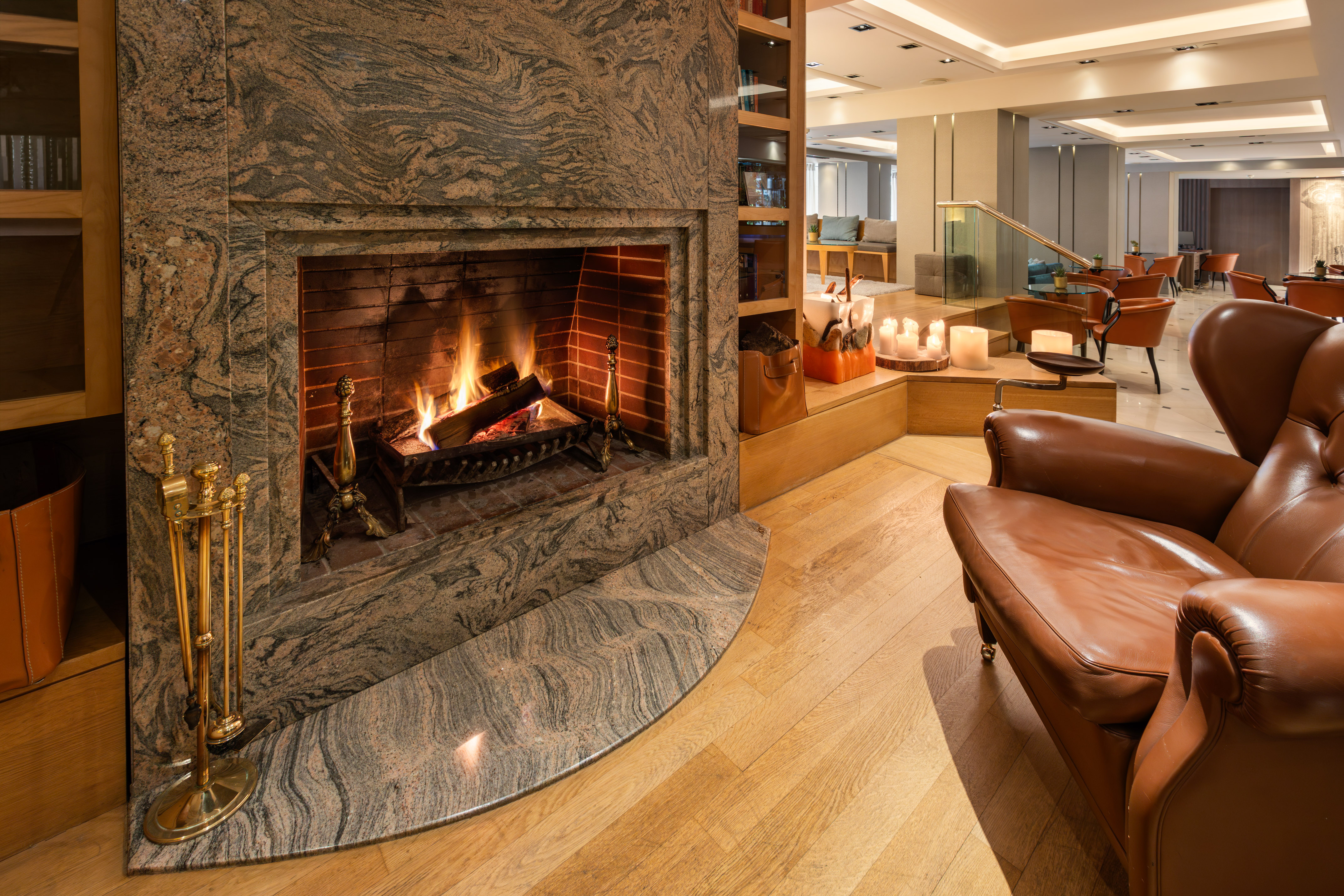 Warm hotel lounge with a marble fireplace, burning logs, and leather armchair.