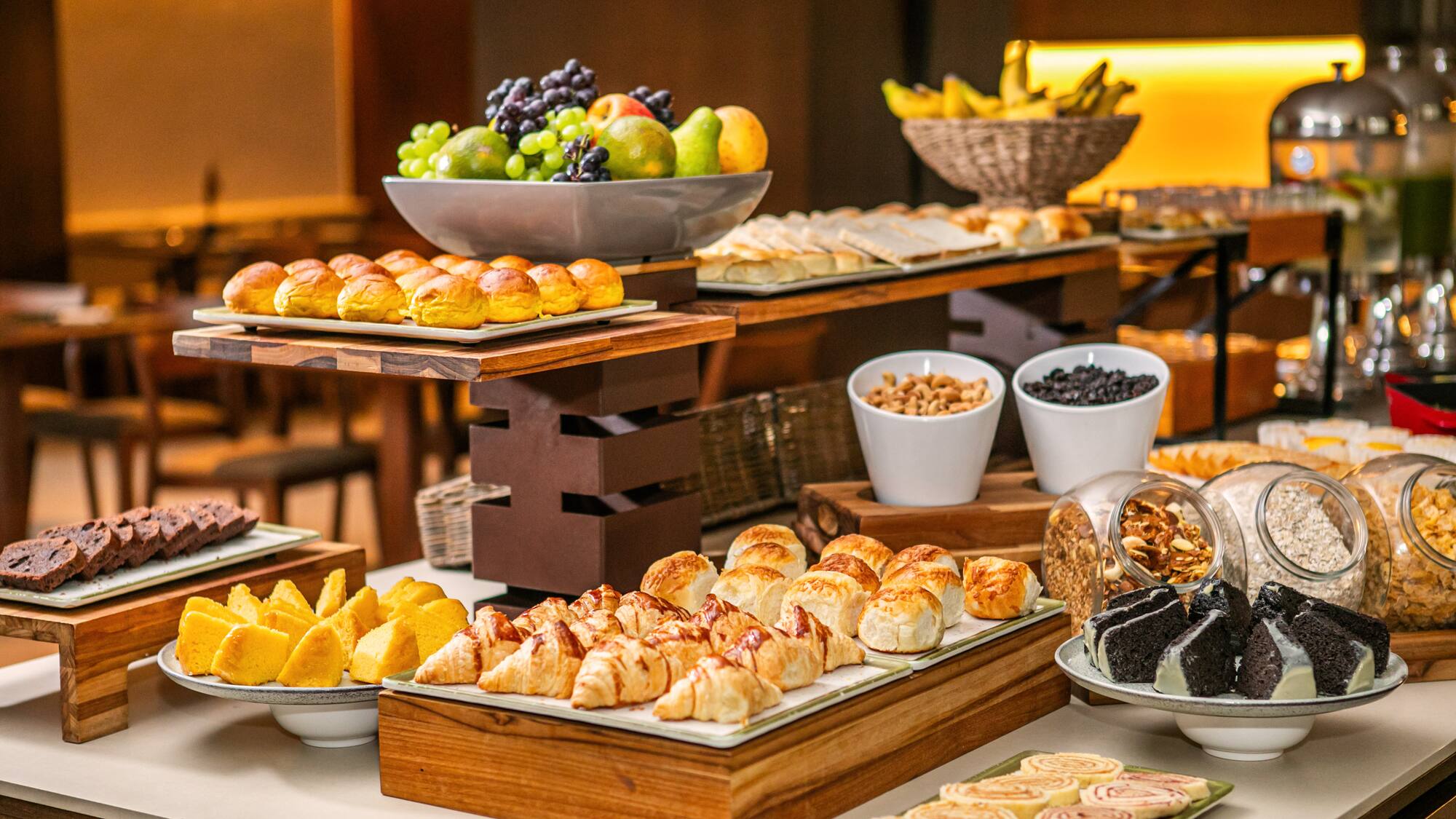 Hotel breakfast buffet with fruit, pastries, croissants, cakes, nuts, and cereals.
