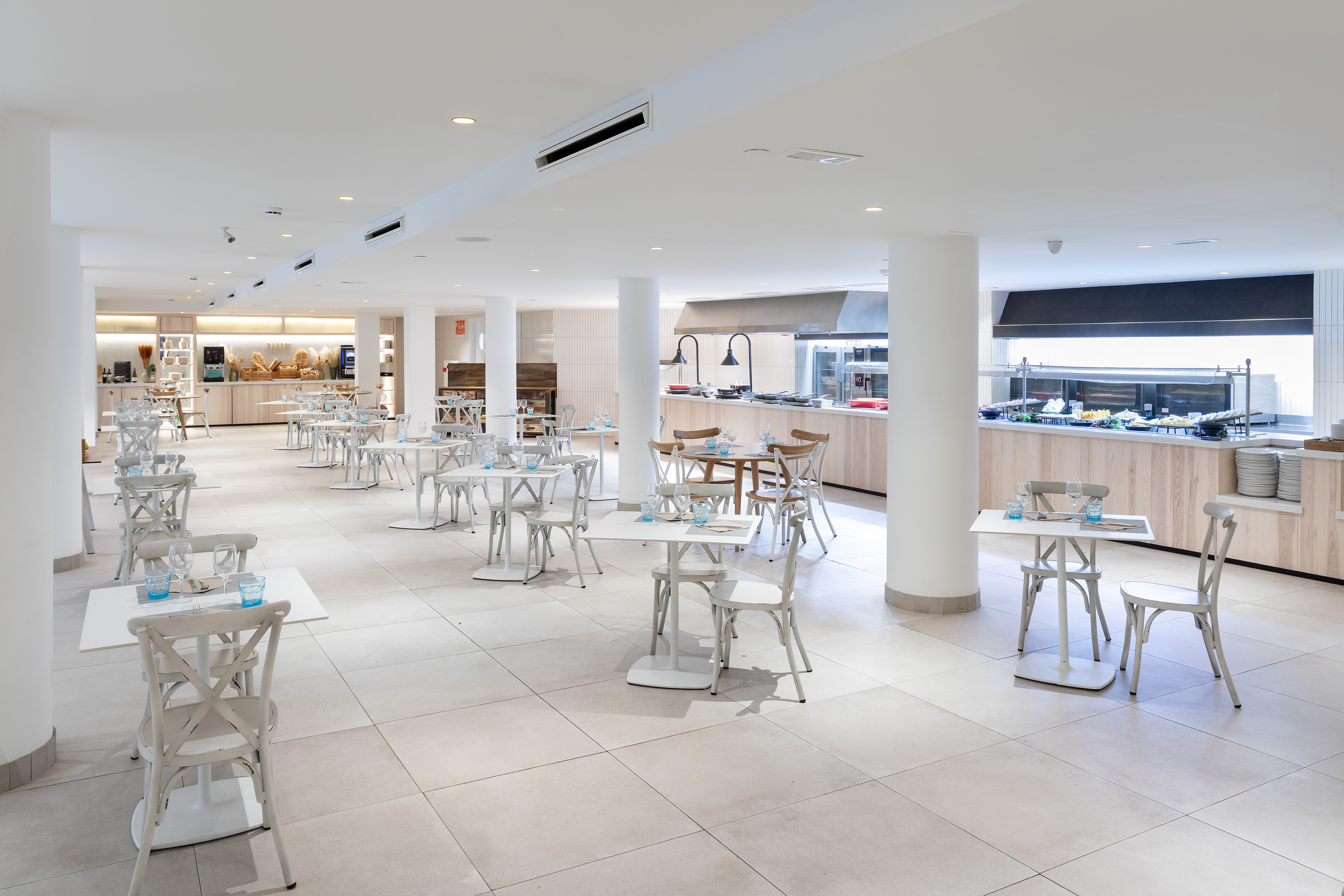 Modern, bright hotel buffet restaurant with tables, chairs, and food stations.