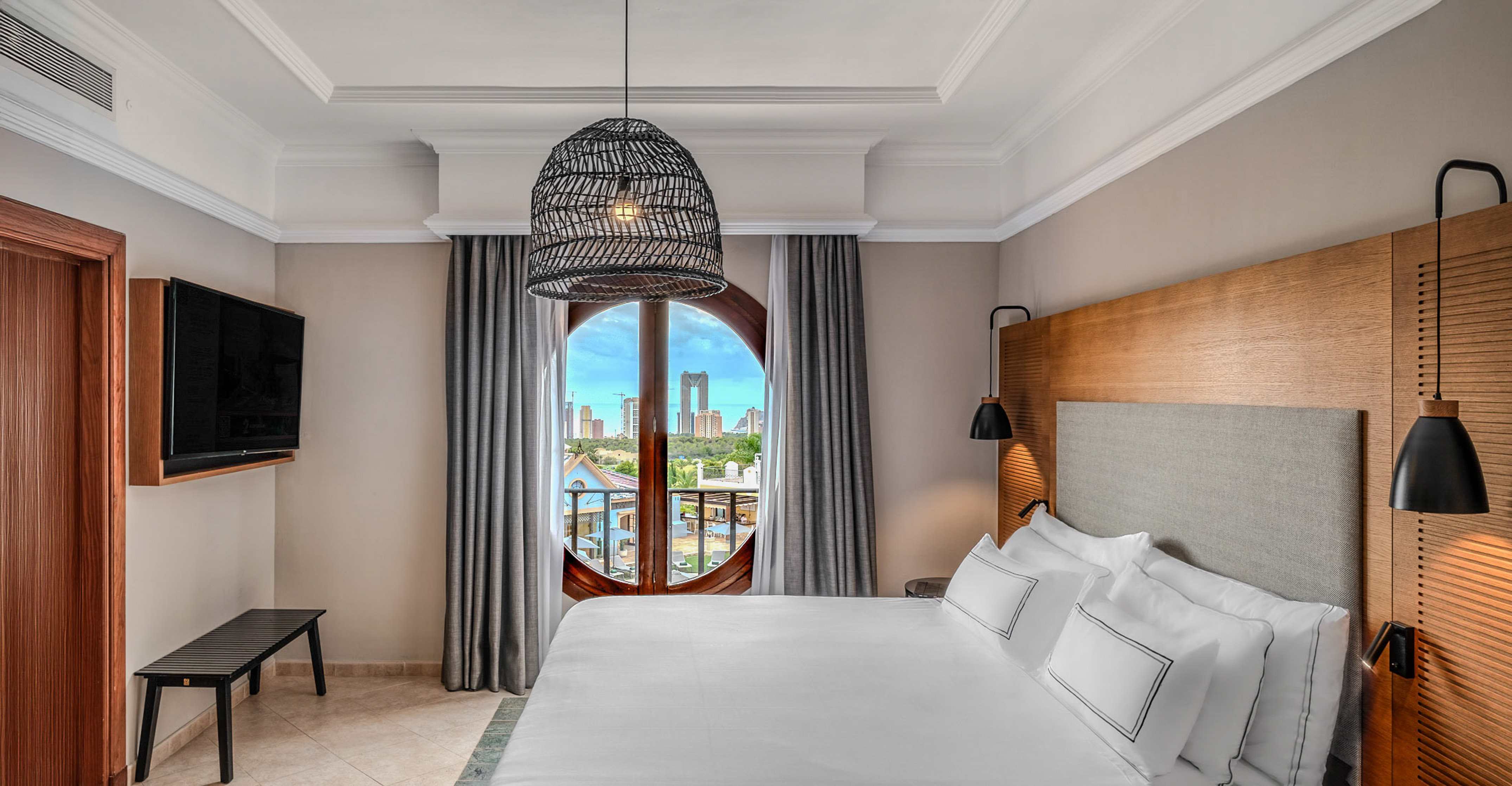 Modern hotel bedroom with city skyline through round window, comfy bed.